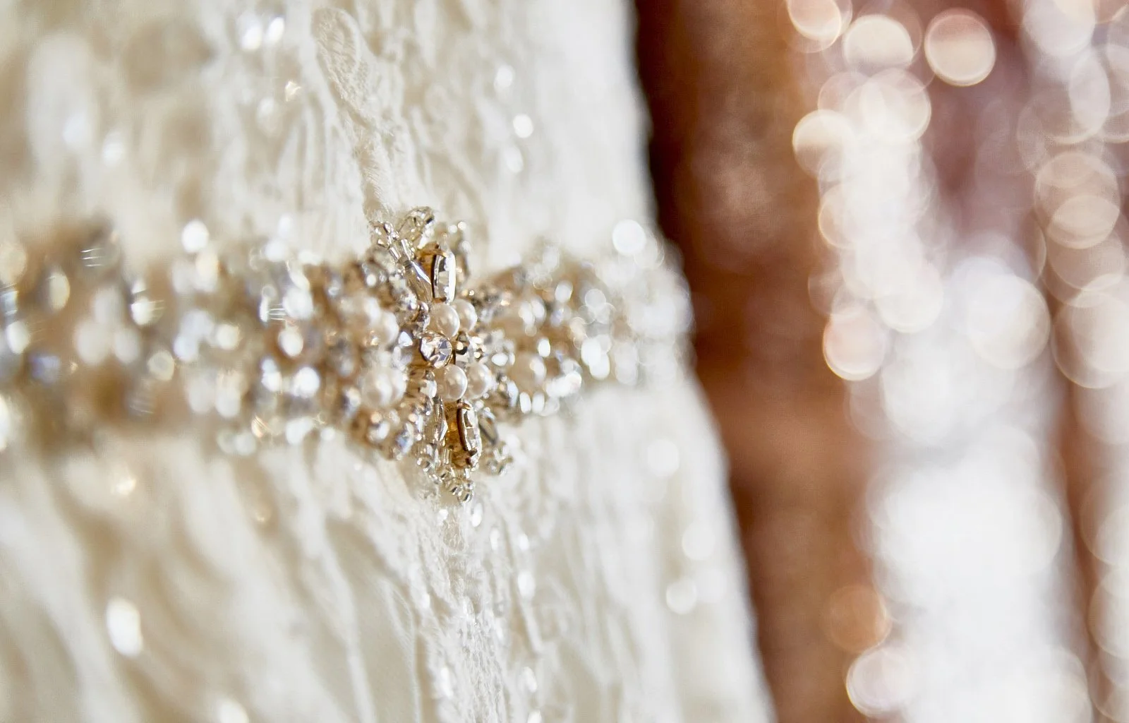 Close-up of a decorative jewelry pin on a textured fabric dress, with a background of blurred warm-colored bokeh lights.