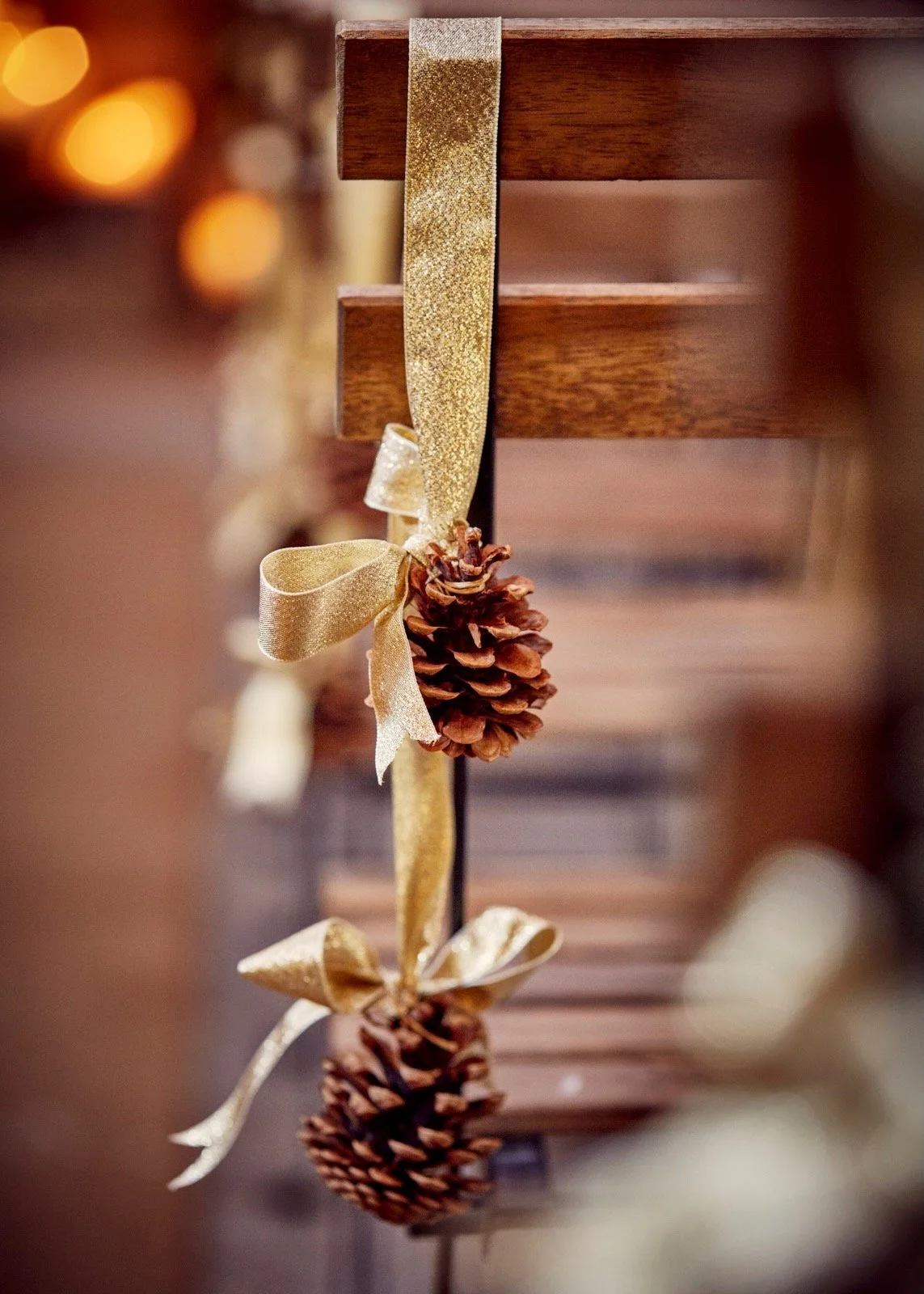 Close-up of a decorative string with pinecones, gold ribbon bows, and gold glitter ribbon draped over a wooden shelf.