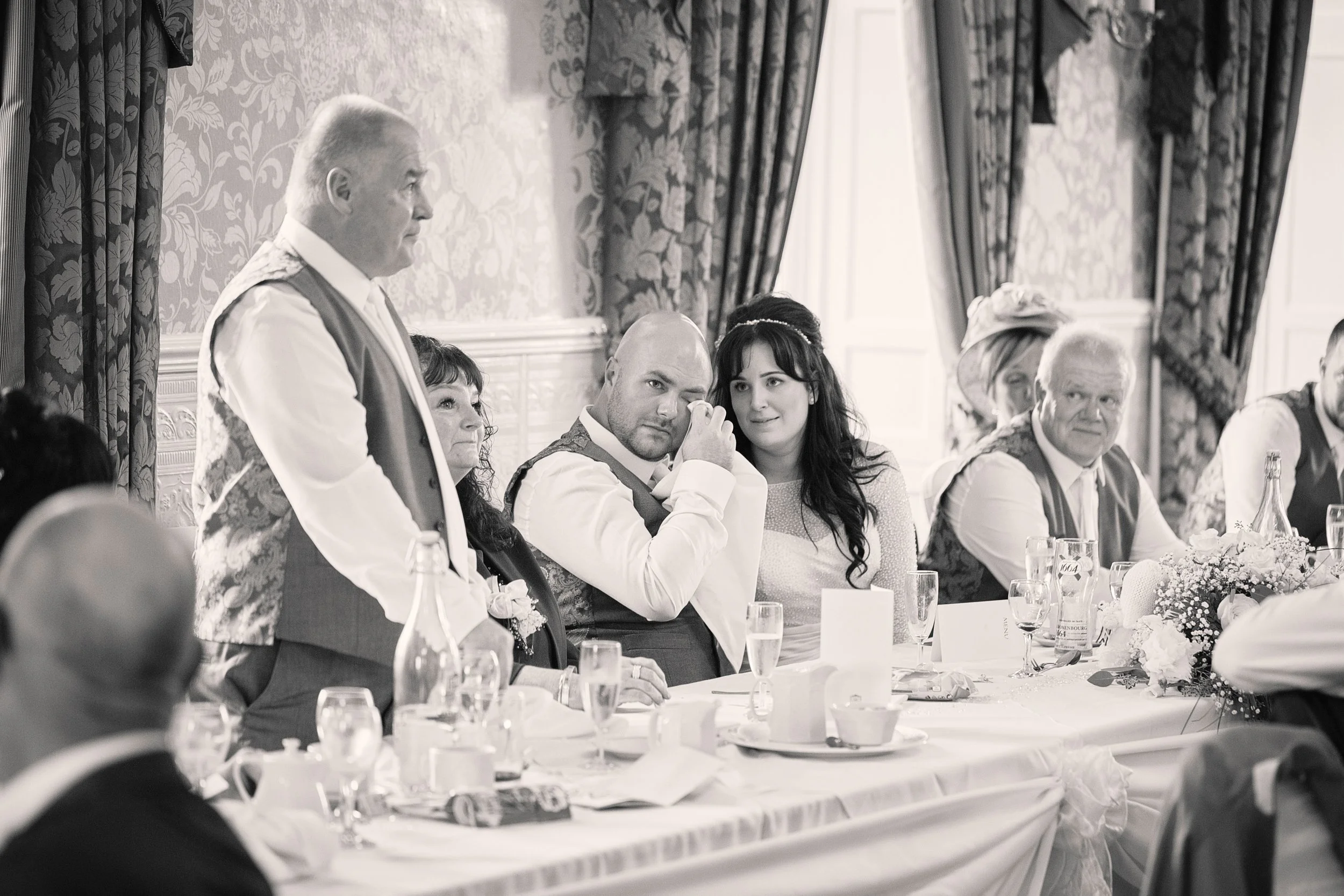 A black and white photo of a formal gathering, with men and women sitting at a long, elegantly decorated table during a celebration or event.