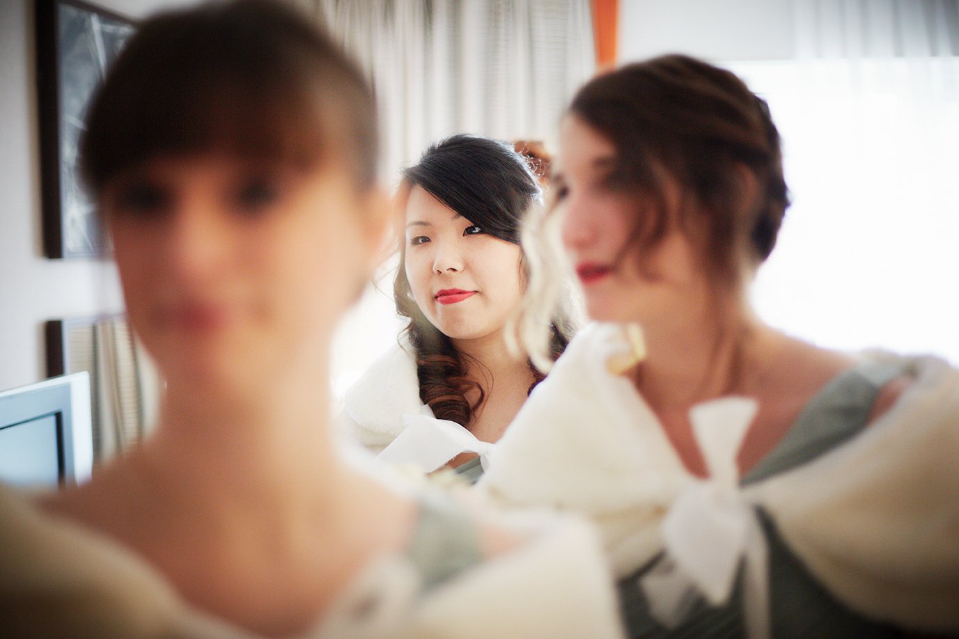 Three women with makeup and dressed in traditional Korean wedding hanbok, preparing for a wedding ceremony.