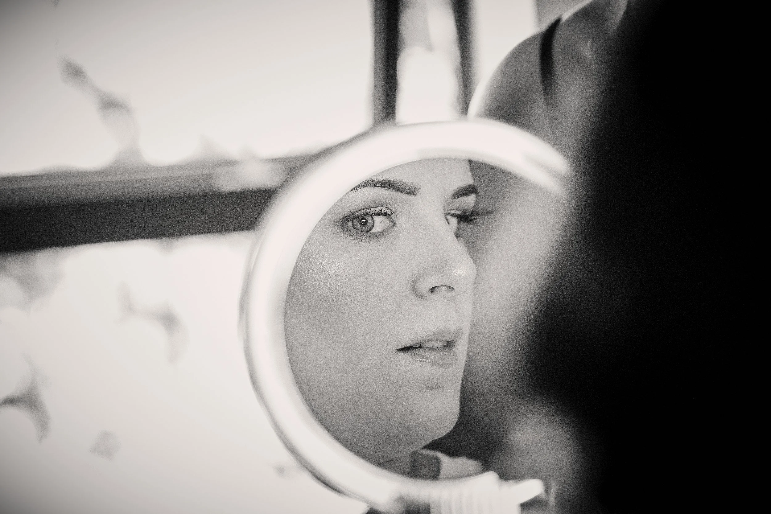 Black and white photo of a woman's face reflected in a circular mirror, focusing on her eyes and lips.