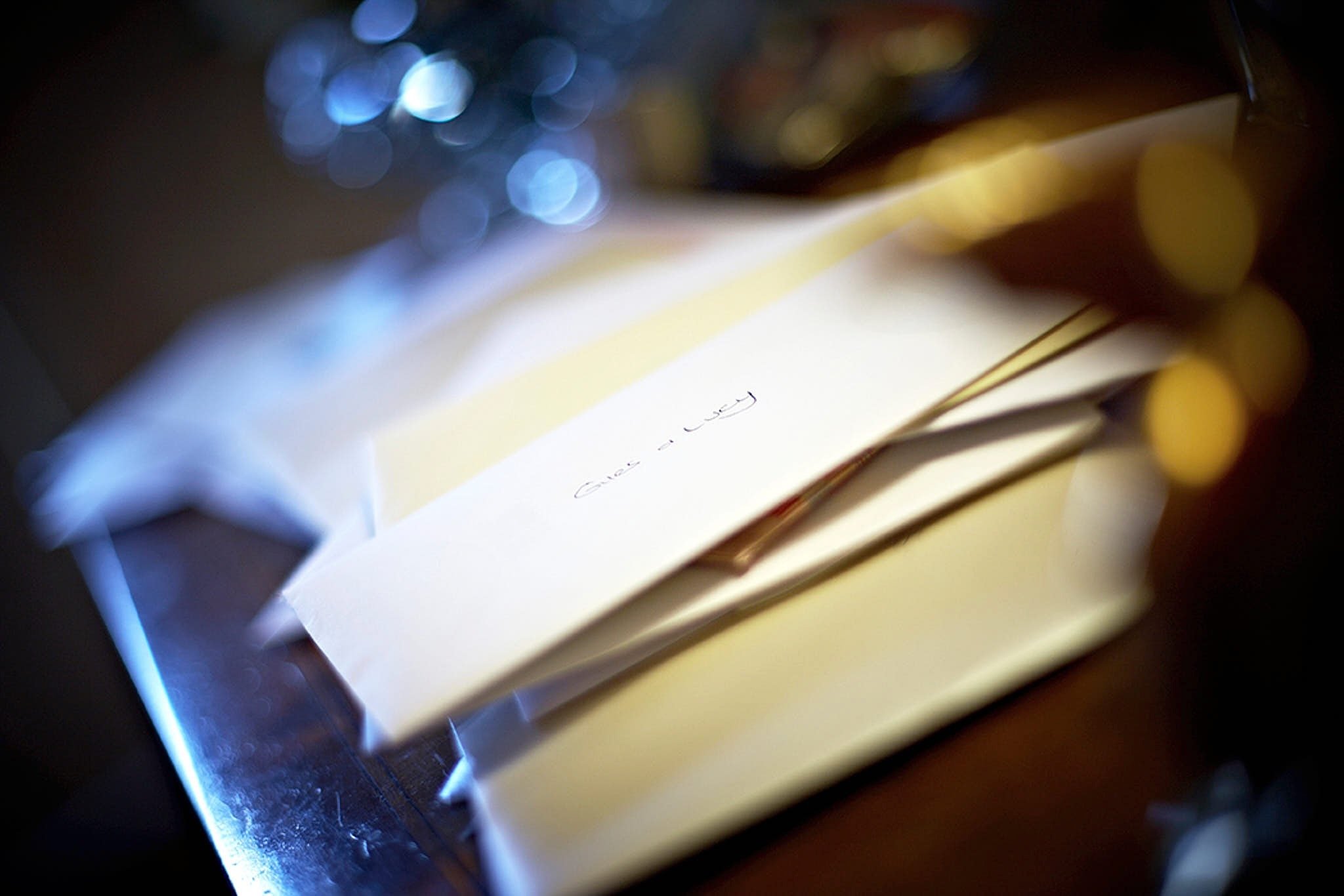 Close-up of stacked papers or files with handwritten text, placed on a dark surface, with out-of-focus blue and white lights in the background.
