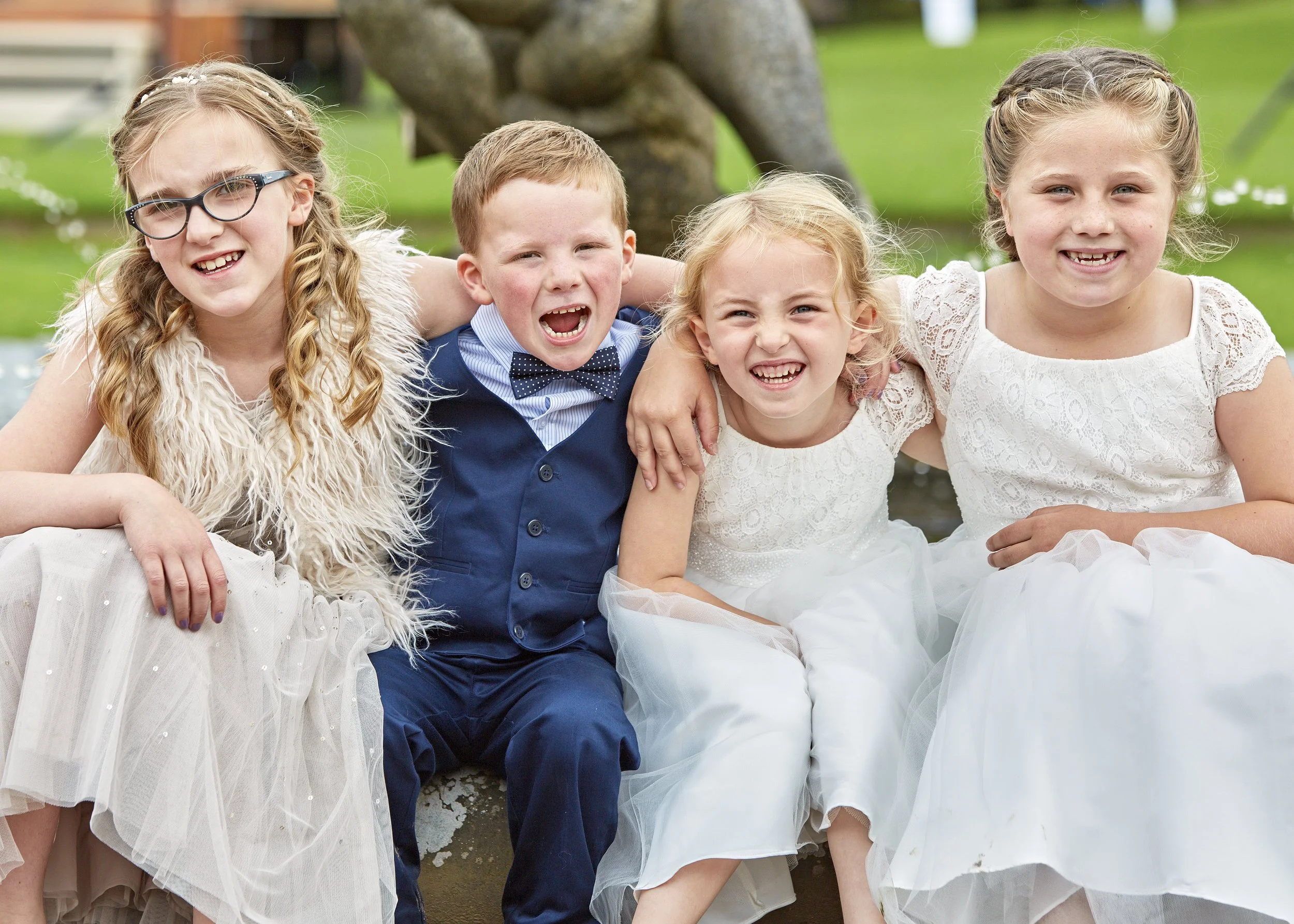 Group of five children sitting outdoors, smiling and laughing, with arms around each other.