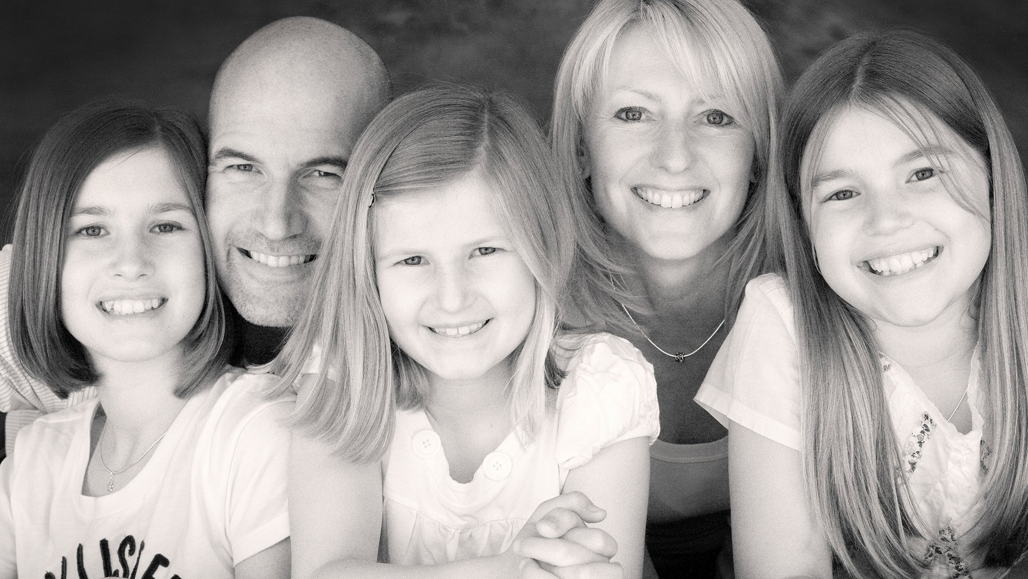 Black and white photograph of a smiling family group including three young girls, an older girl, a woman, and a man, all close together.