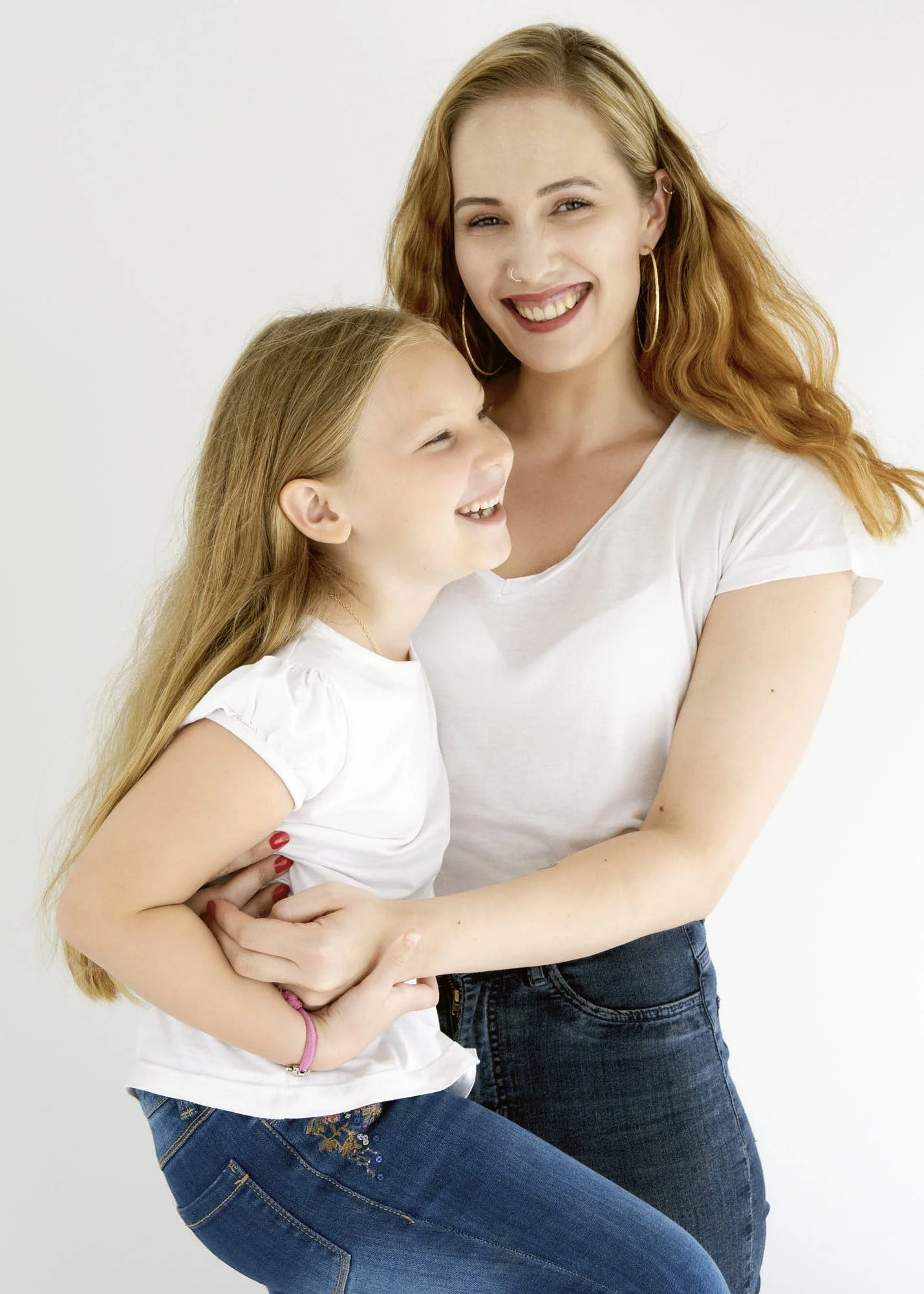 A red-haired woman and a young girl hugging, both smiling in front of a plain white background.