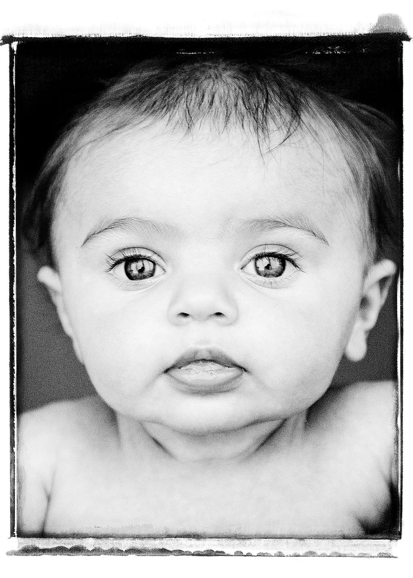 Black and white photograph of a young child's face with large, bright eyes and a small, slightly open mouth, looking directly at the camera.
