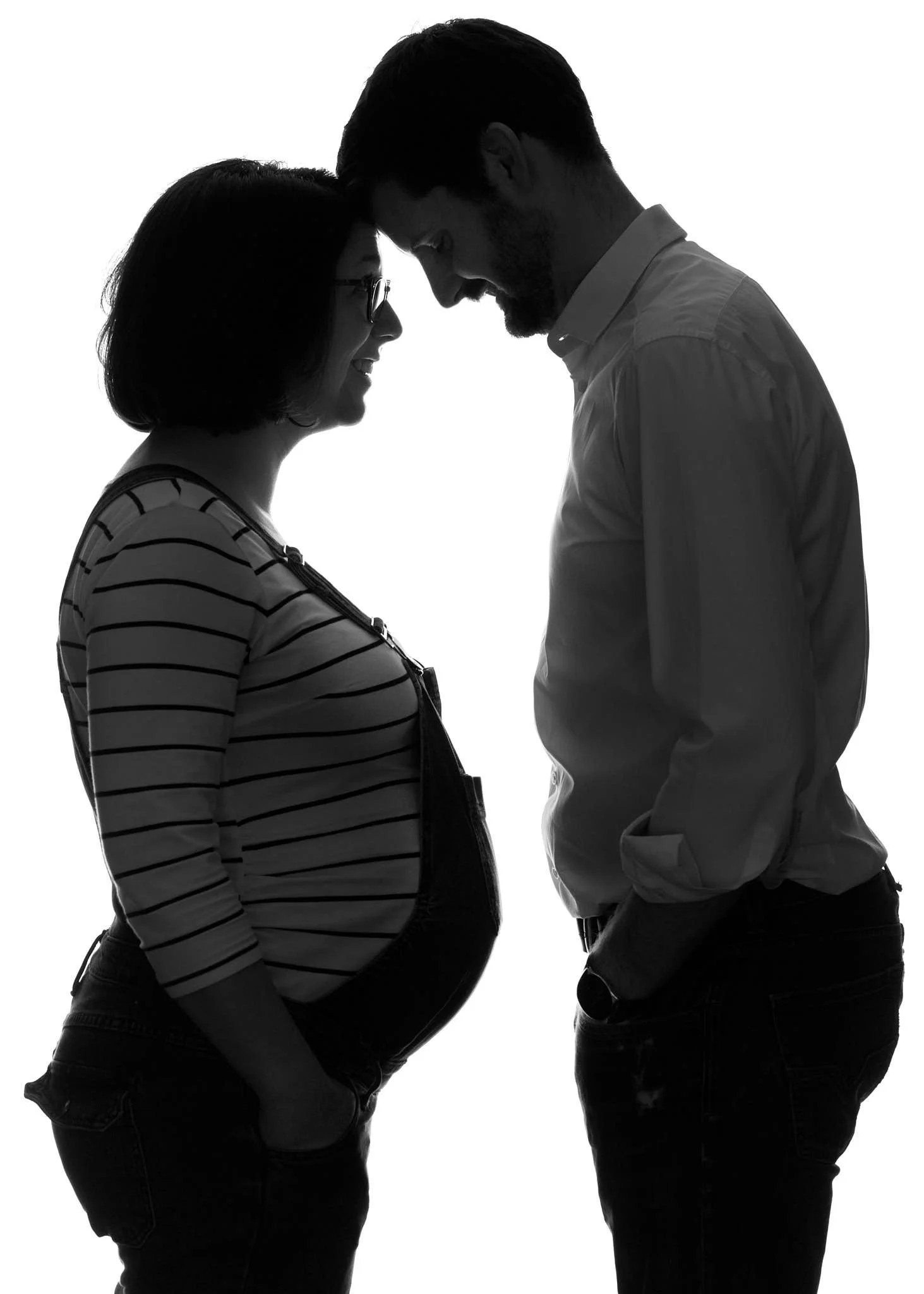 Silhouette of a pregnant woman and a man with foreheads touching, smiling, facing each other, in black and white.