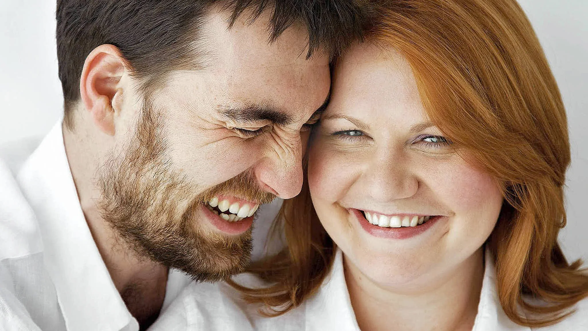 Close-up of a happy couple smiling and sharing a moment, with the man on the left and the woman on the right.