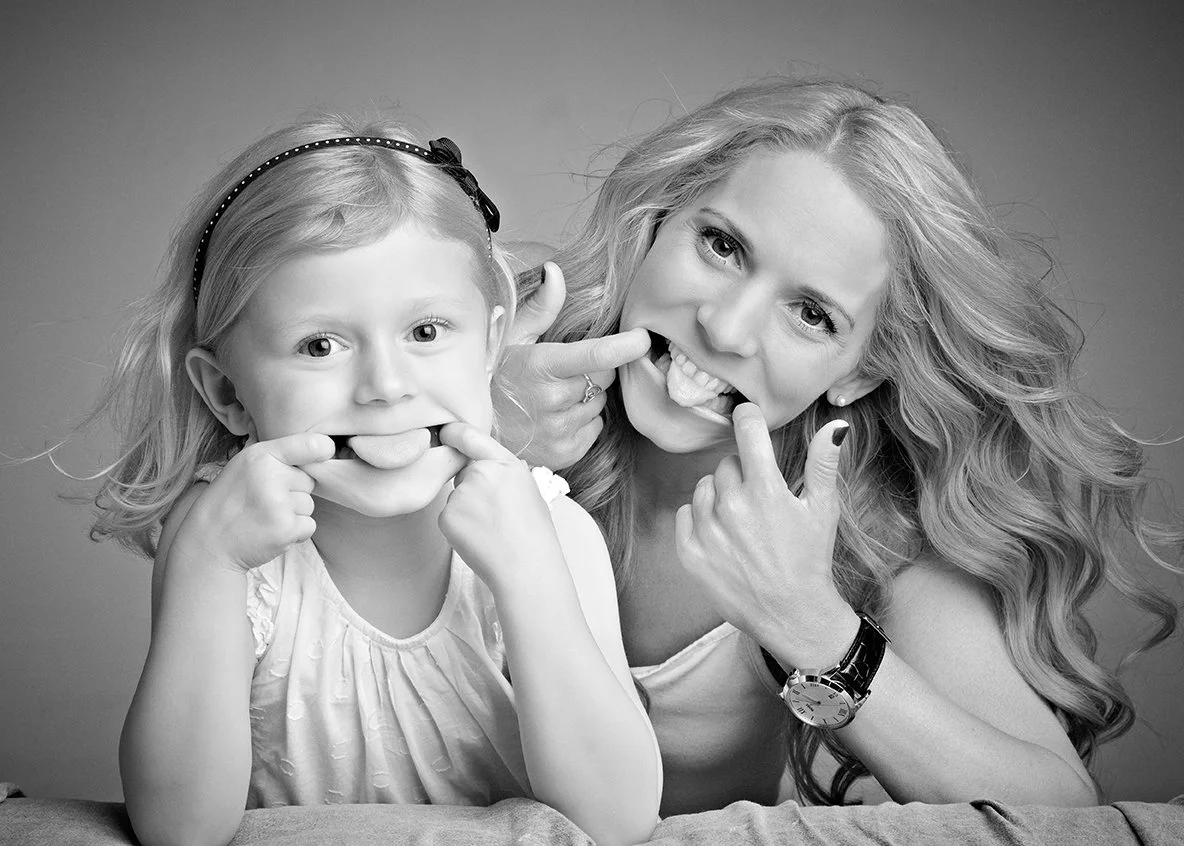 A woman and a young girl making silly faces with their fingers in their mouths.