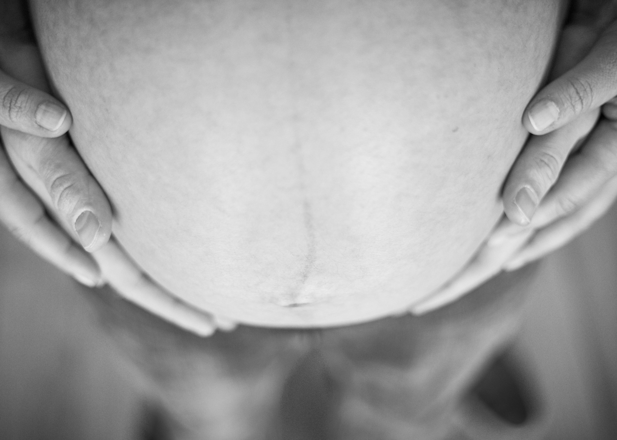 Close-up black-and-white photo of a person's stomach with hands holding the sides of their abdomen.