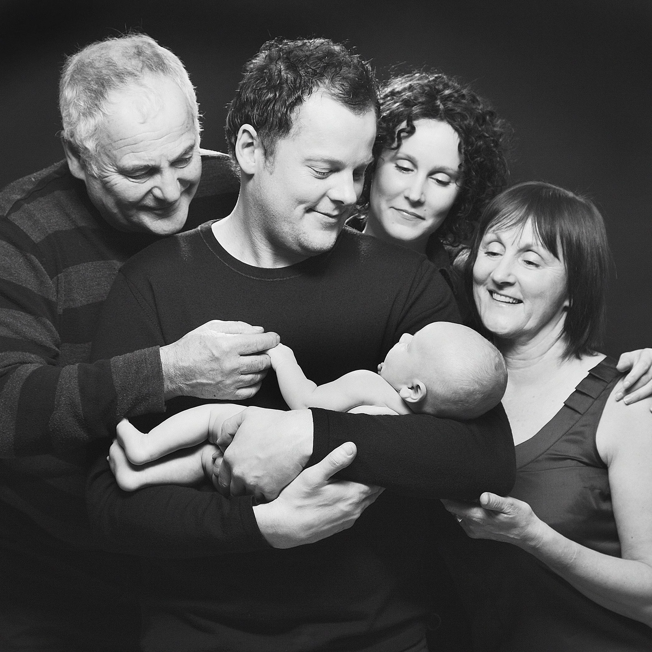 Black and white photo of five people, with close-cropped headshots, embracing each other in a group hug, all smiling warmly.