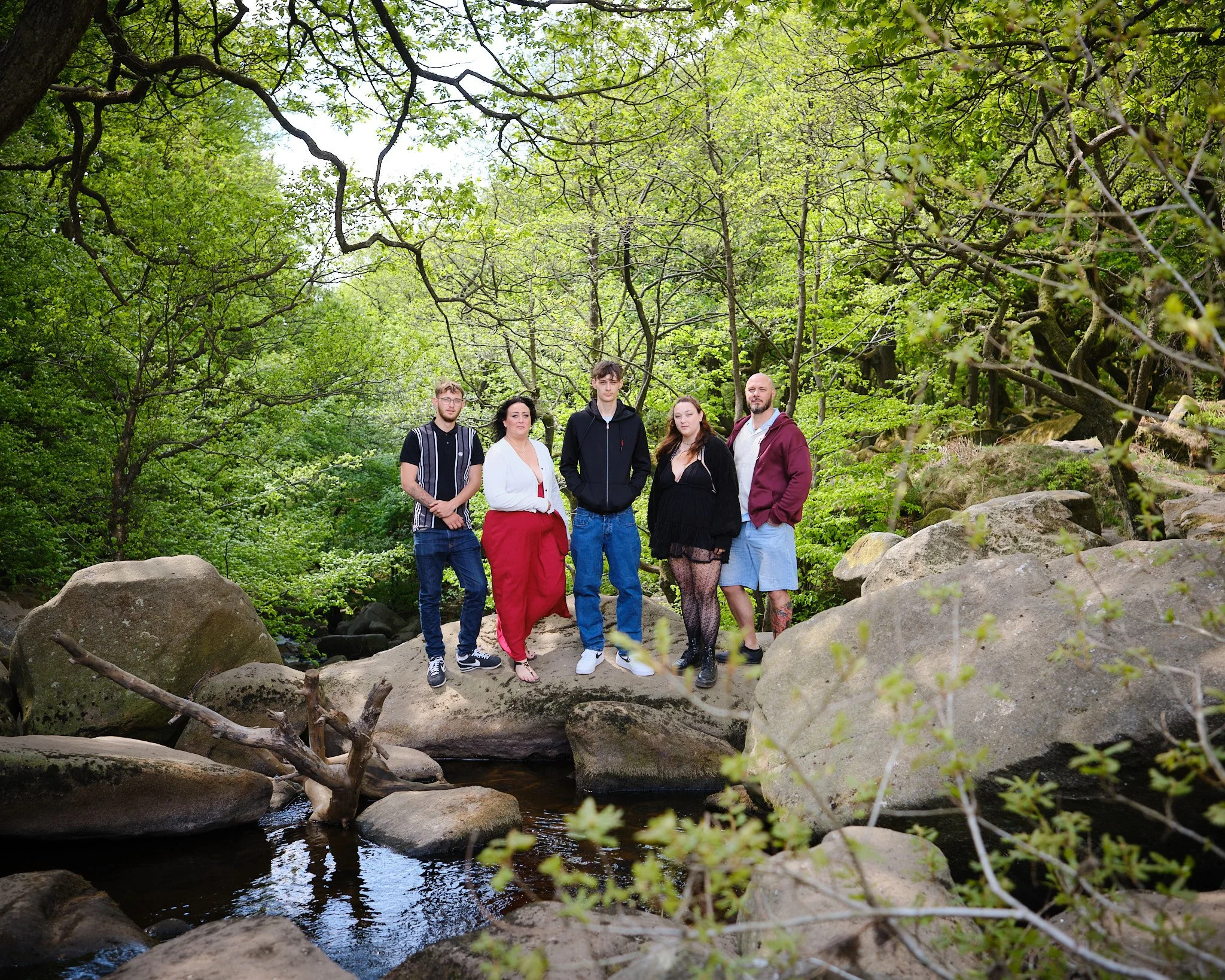 Group of five People posing on a rocky creek bed surrounded by trees in a lush forest.