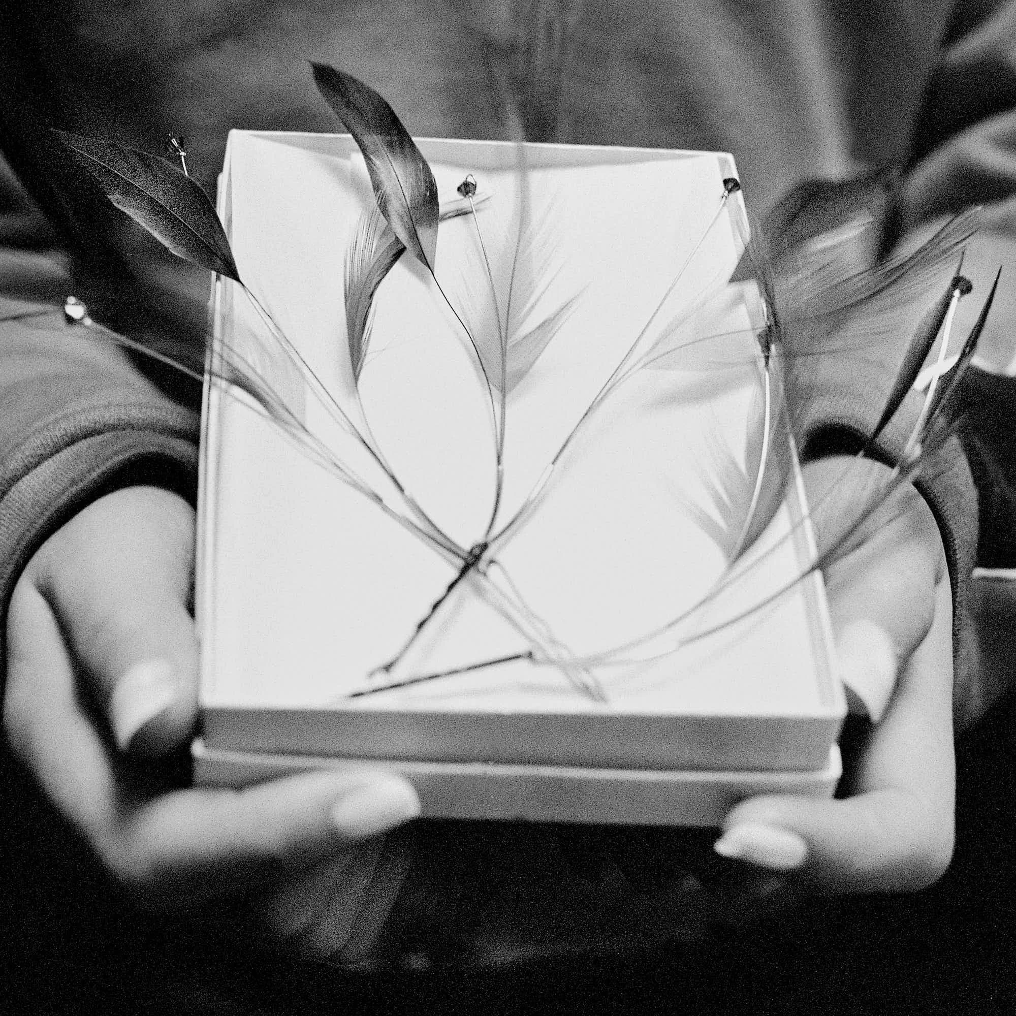 Black and white photo of a person holding an open notebook with handwritten notes, with several feathers placed in the notebook.