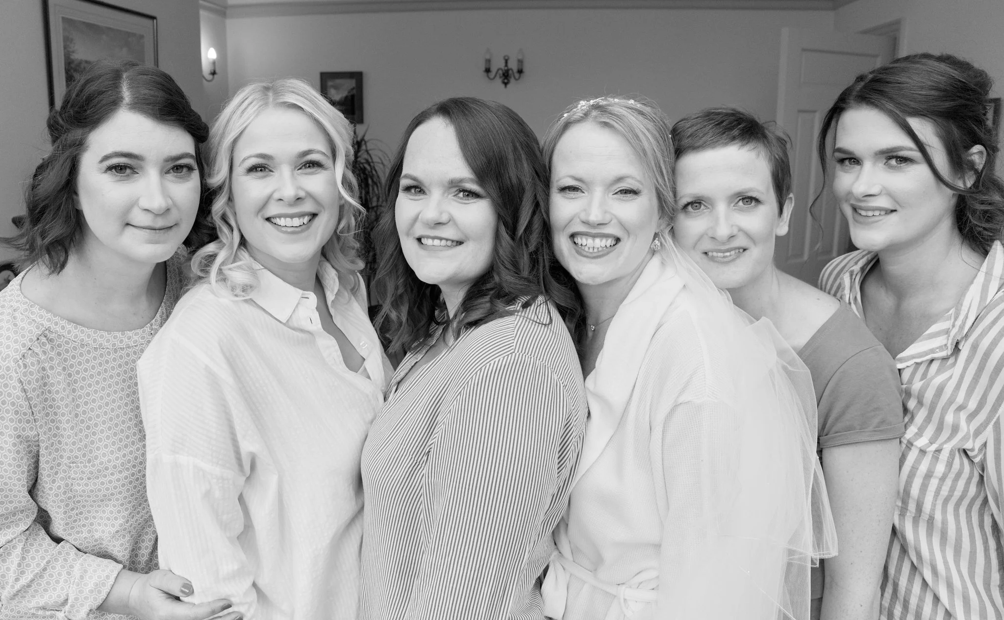 A black and white photo of seven smiling women standing close together indoors.
