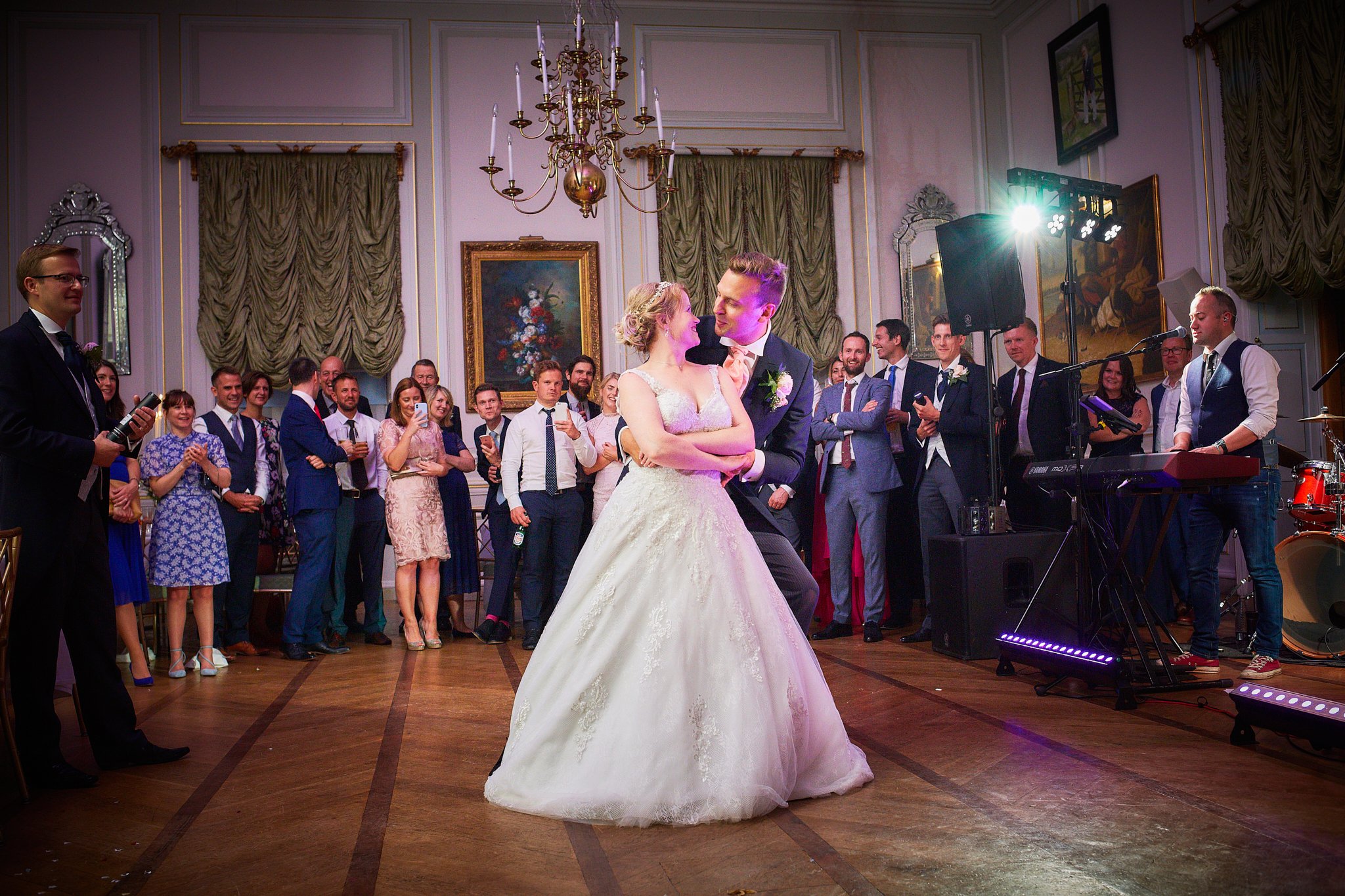 A bride and groom dancing at their wedding reception with friends and family gathered around watching.