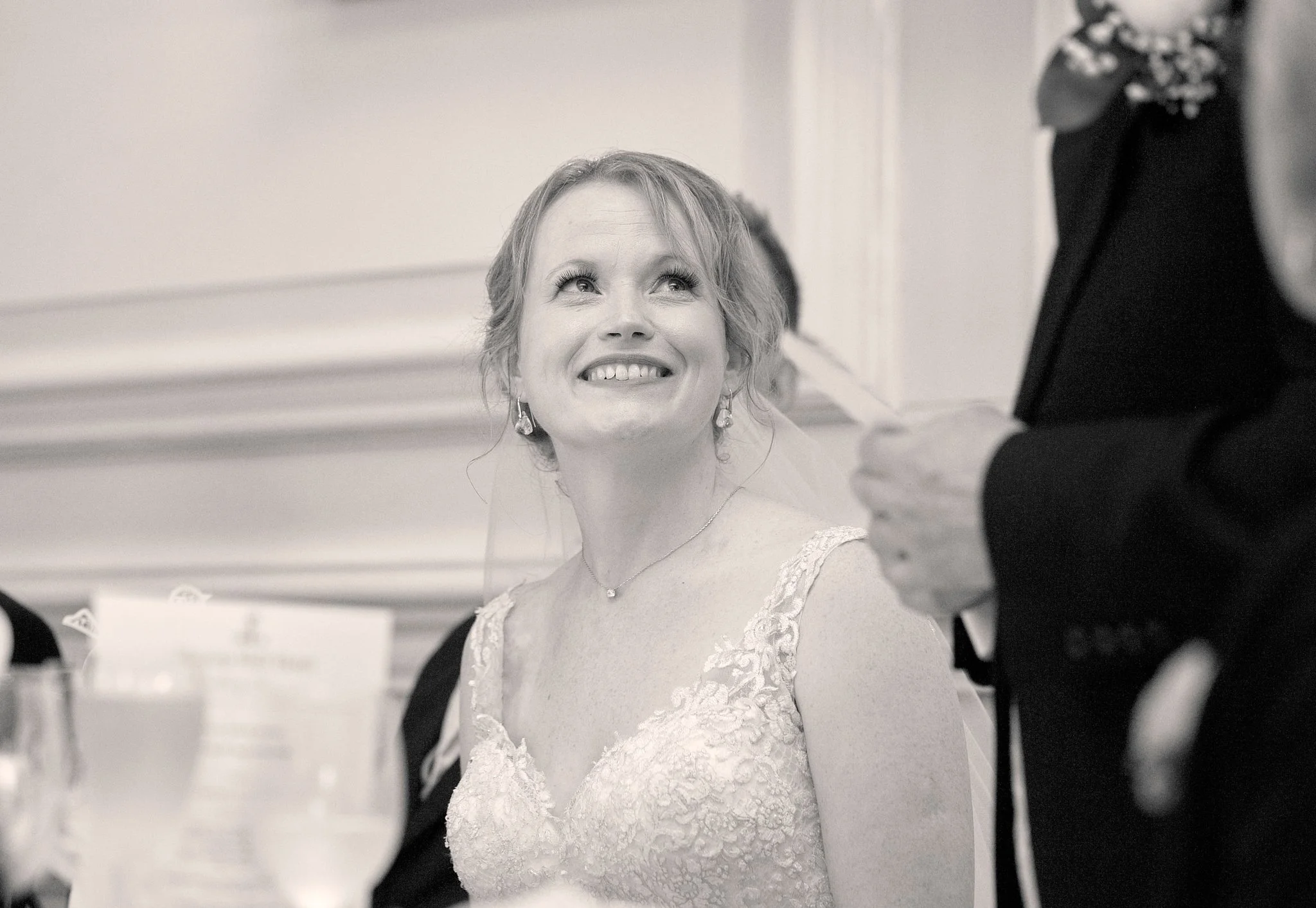 A woman with light hair and earrings looking up at a man in a black suit with a flower boutonniere, smiling.