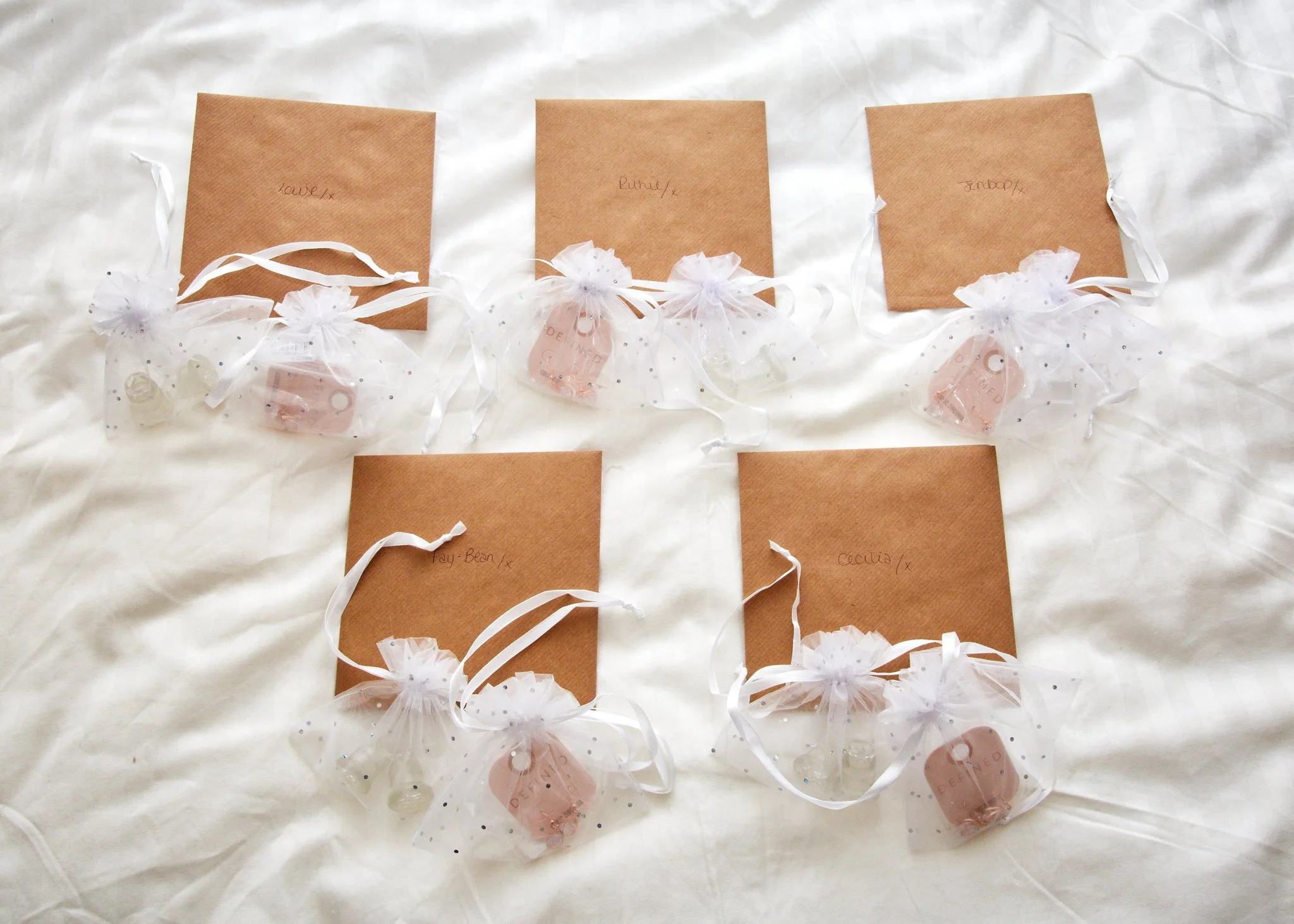 Several small gift bags with white ribbons and tissue paper, each labeled with a name, arranged on a white surface.