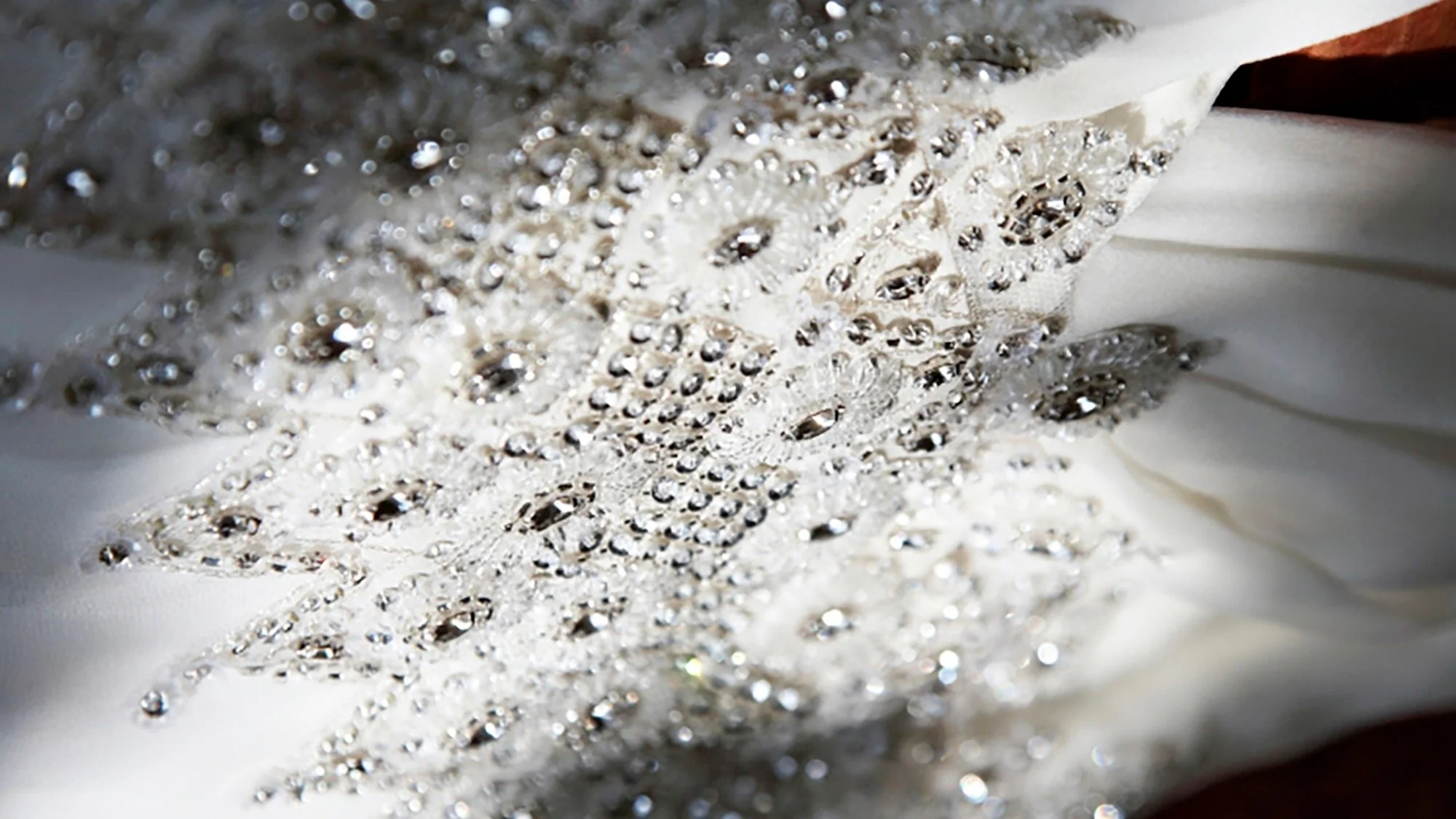 Close-up of silver and white lace fabric embellished with shimmering rhinestones or beads, creating an intricate and elegant pattern.