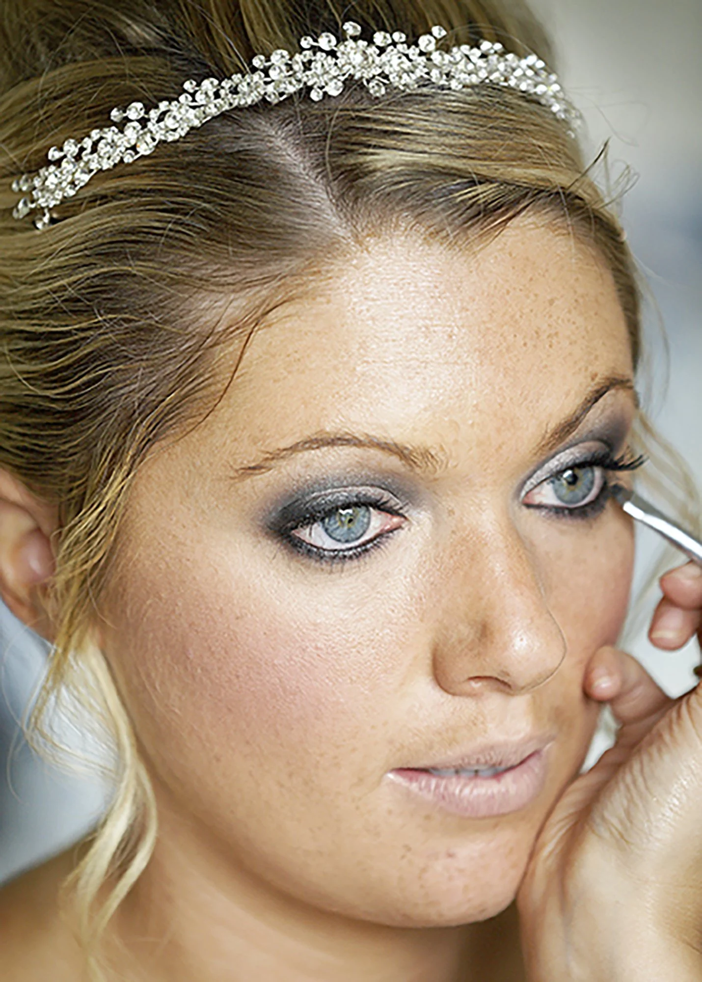 Close-up of a woman with blonde hair, blue eyes, and makeup, wearing a rhinestone headband.