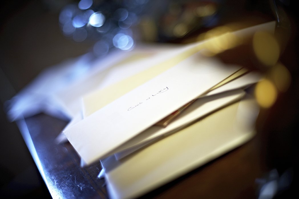 A stack of white envelopes on a dark wooden surface with some bokeh lights in the background.
