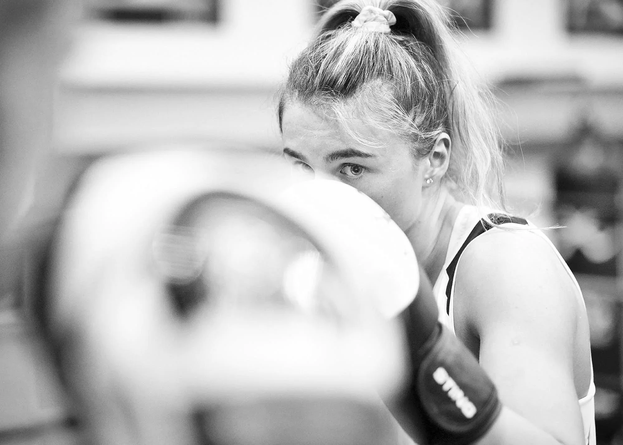 A young woman with light hair tied in a ponytail, wearing sports attire, practicing boxing or boxing training with focus and intensity.