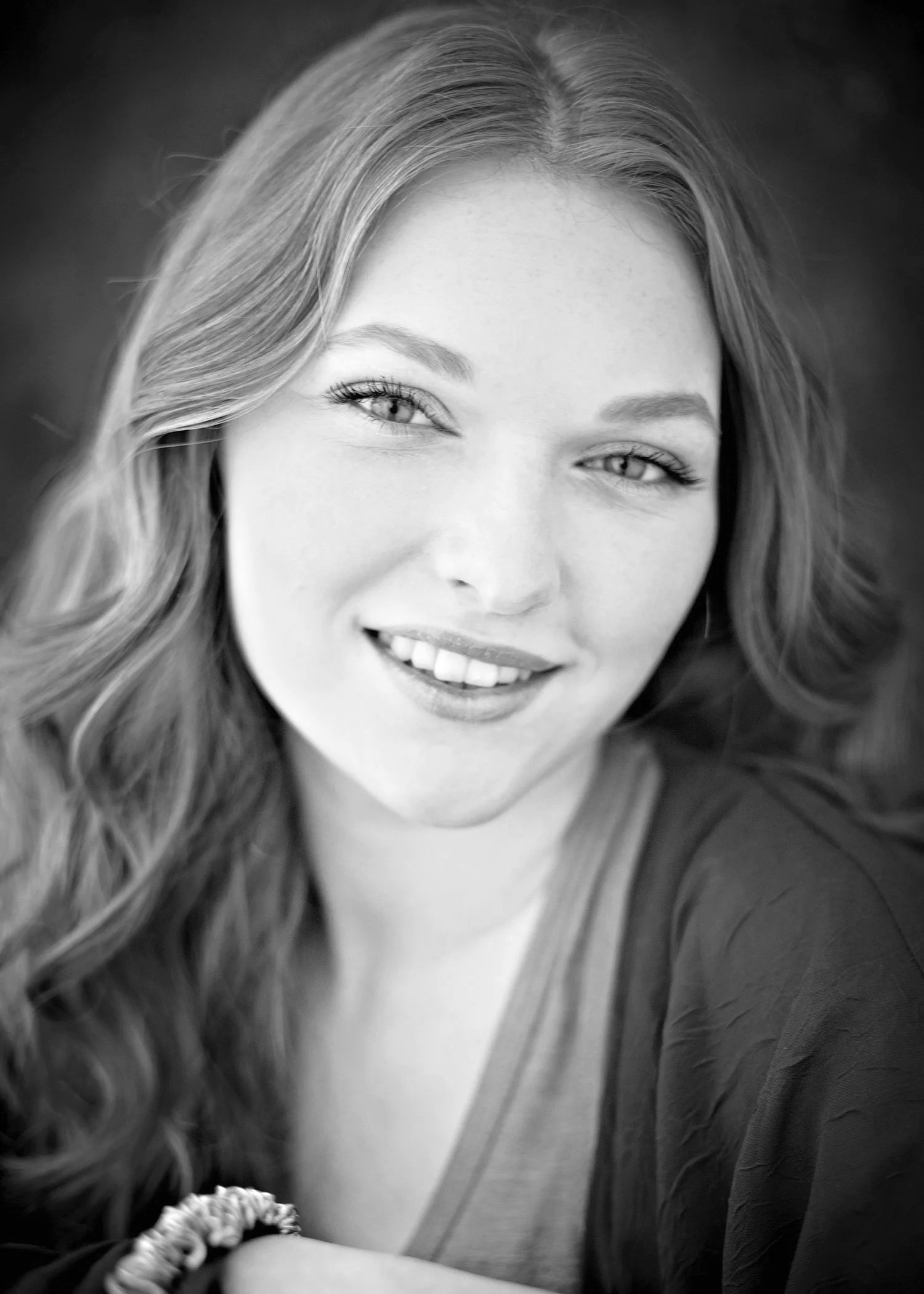 Black and white close-up portrait of a smiling woman with long, wavy hair and light-colored eyes.