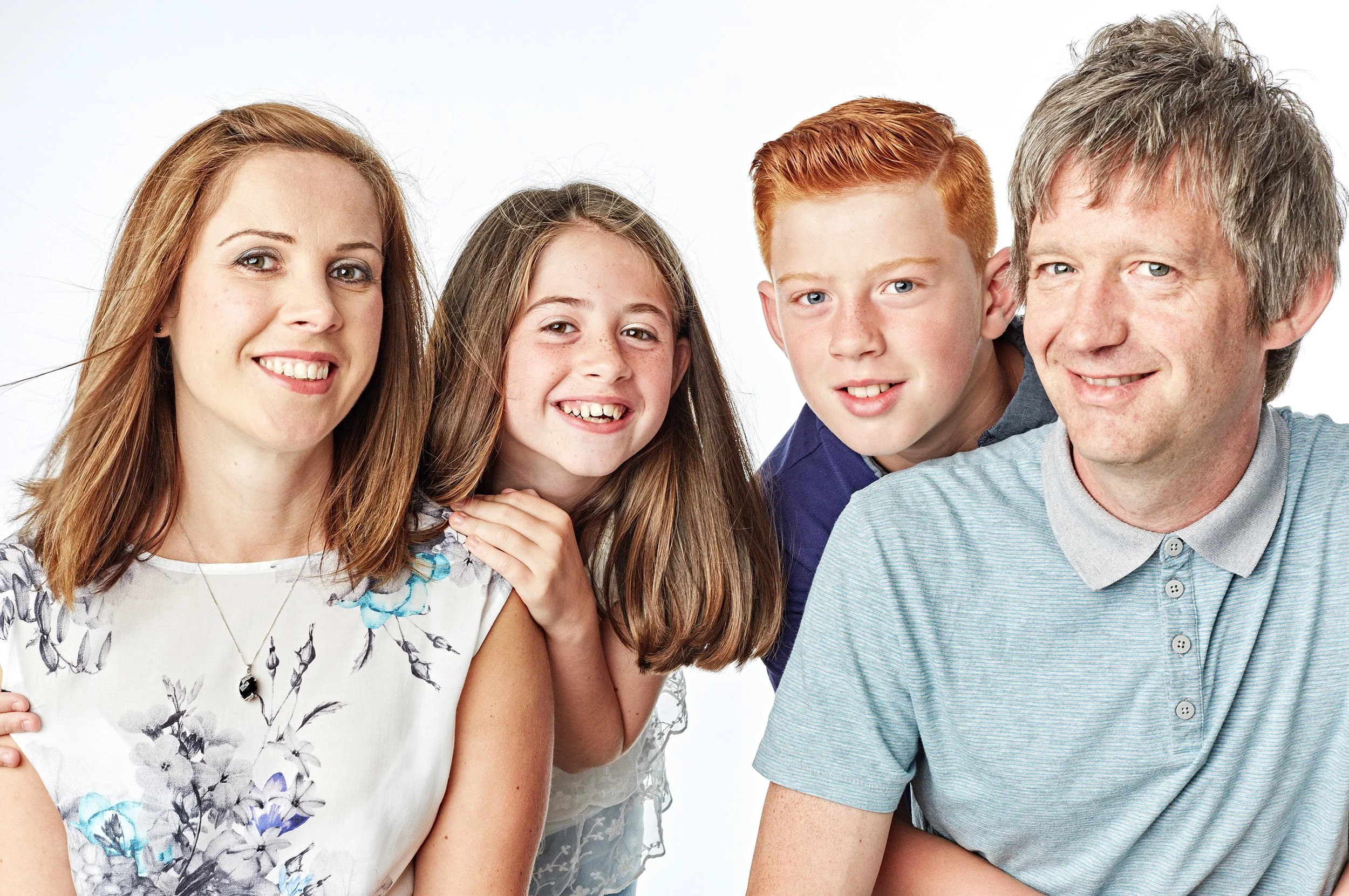 A family of five posing together, with three children and two adults, all smiling, against a plain white background.