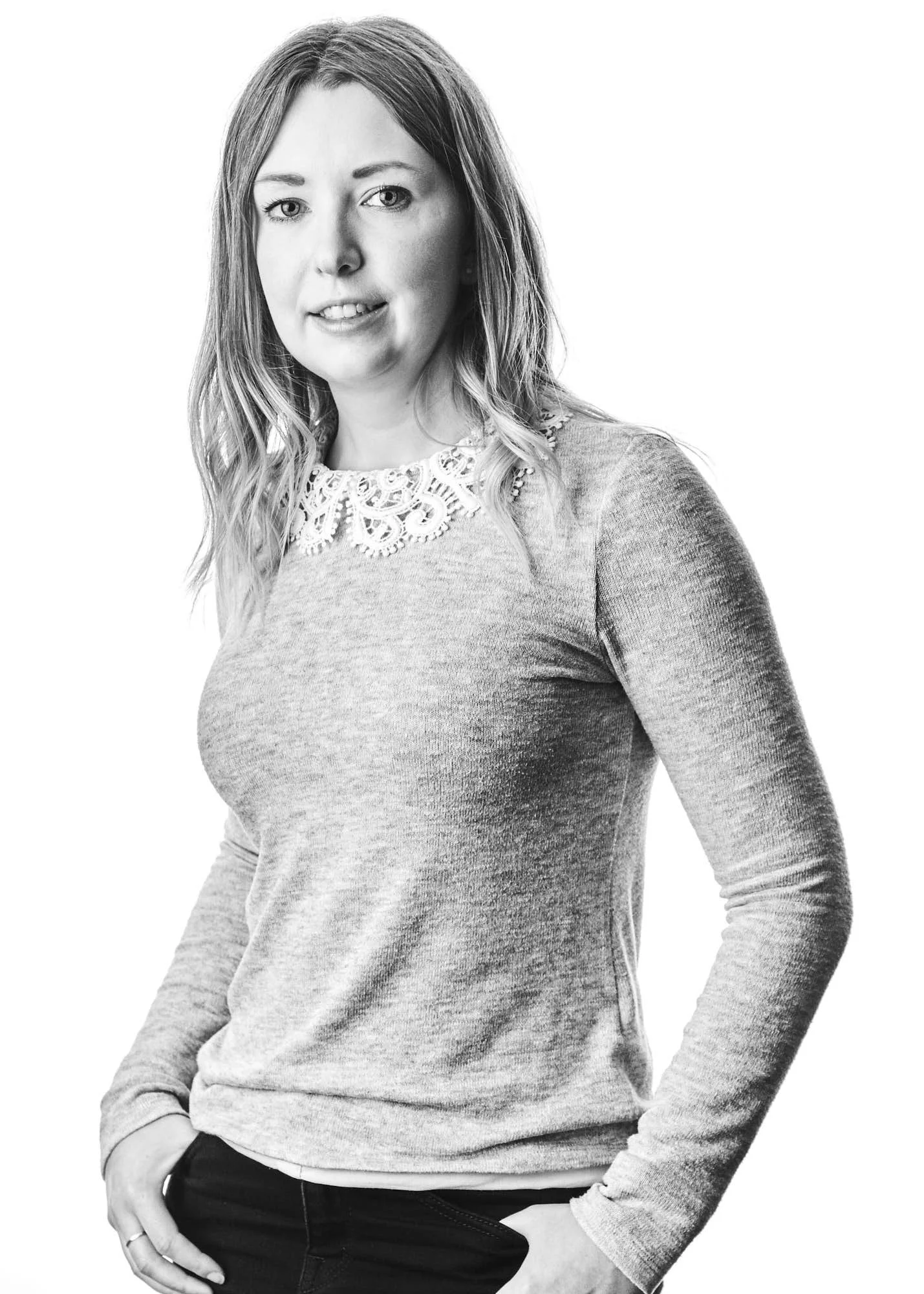 A woman with long hair wearing a long-sleeve shirt with lace details around the collar, standing with her right hand in her pocket in a black-and-white photo.