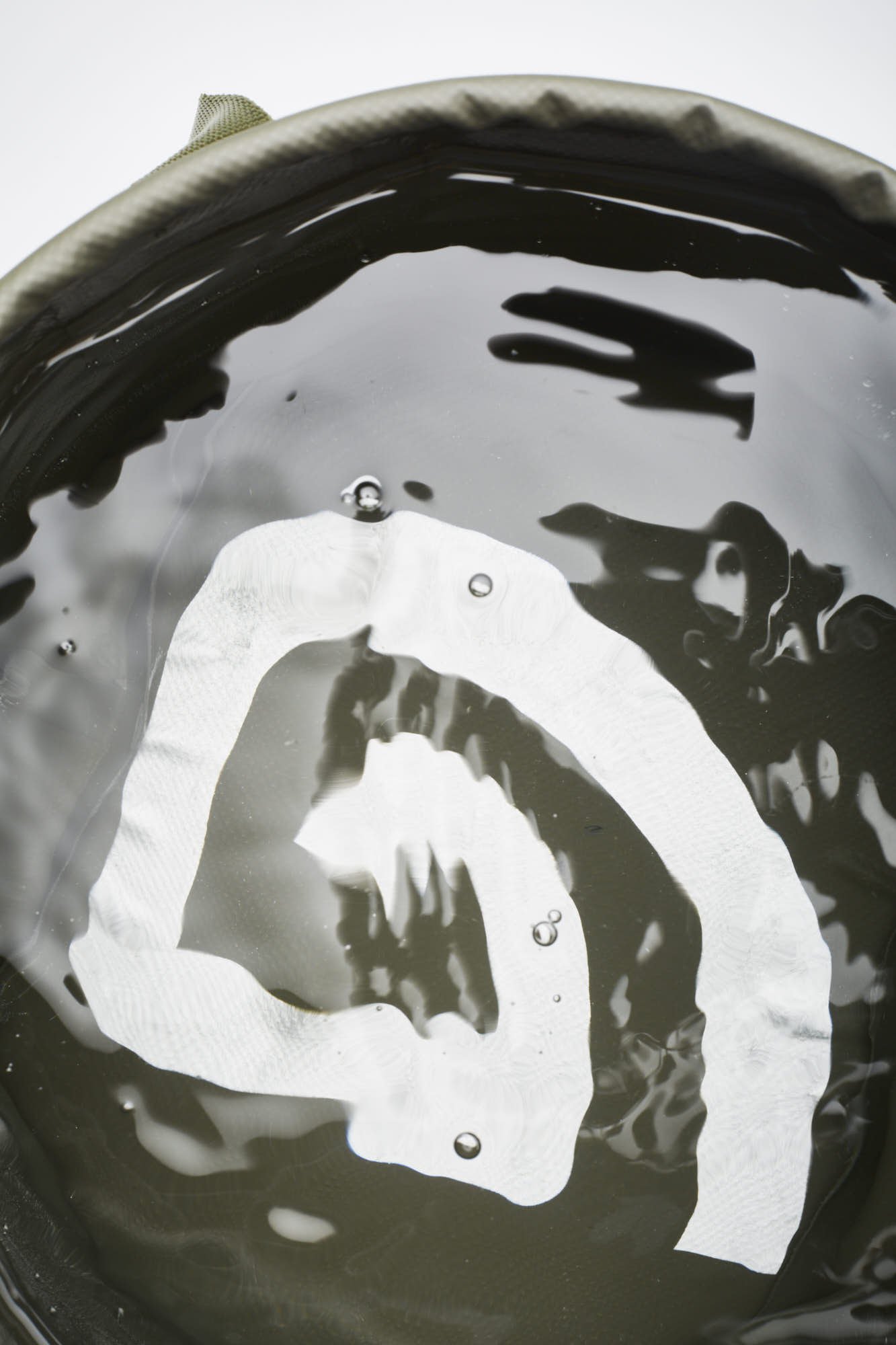 Close-up of a black cooking pot with a silver object inside, reflecting the surroundings, with bubbles and a shiny surface.