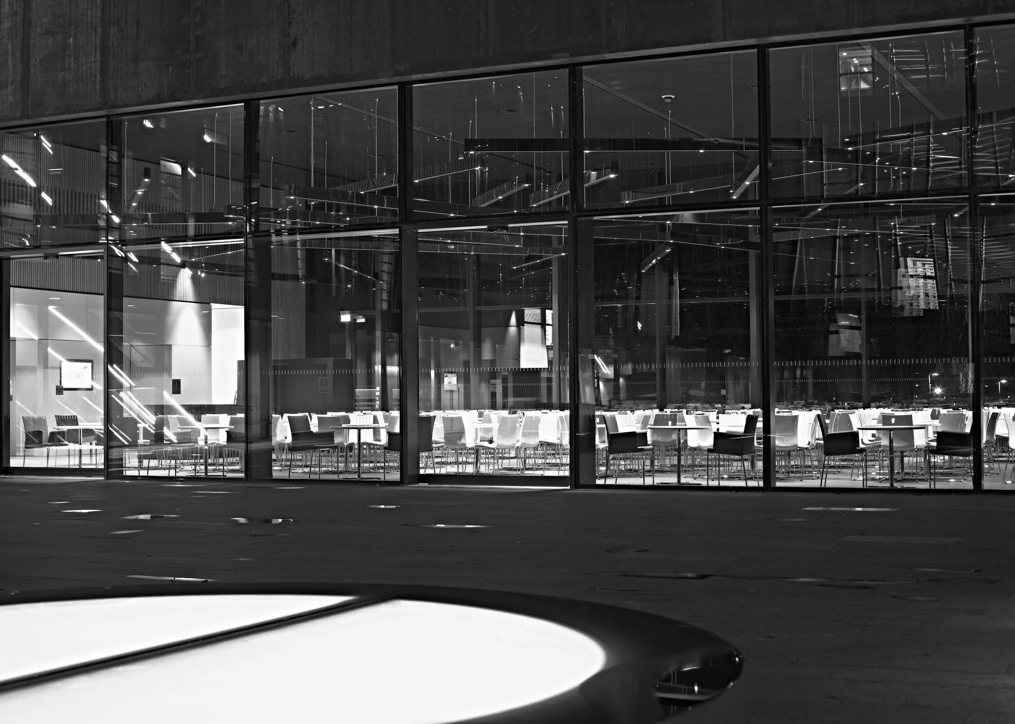A modern, glass-fronted building with illuminated interior seating, viewed at night from the parking lot.