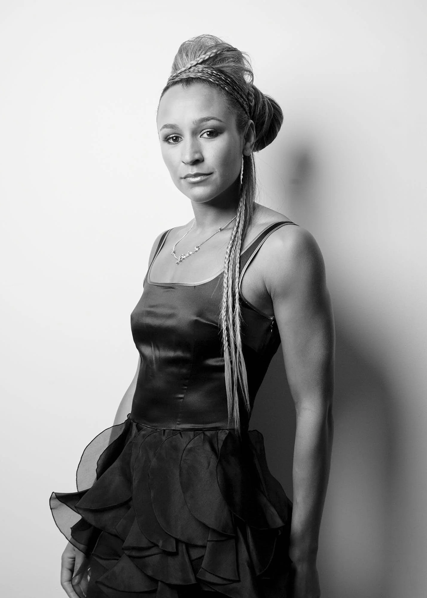 Black and white portrait of a woman with braided hair in an elegant dress, sitting on a chair, looking at the camera.