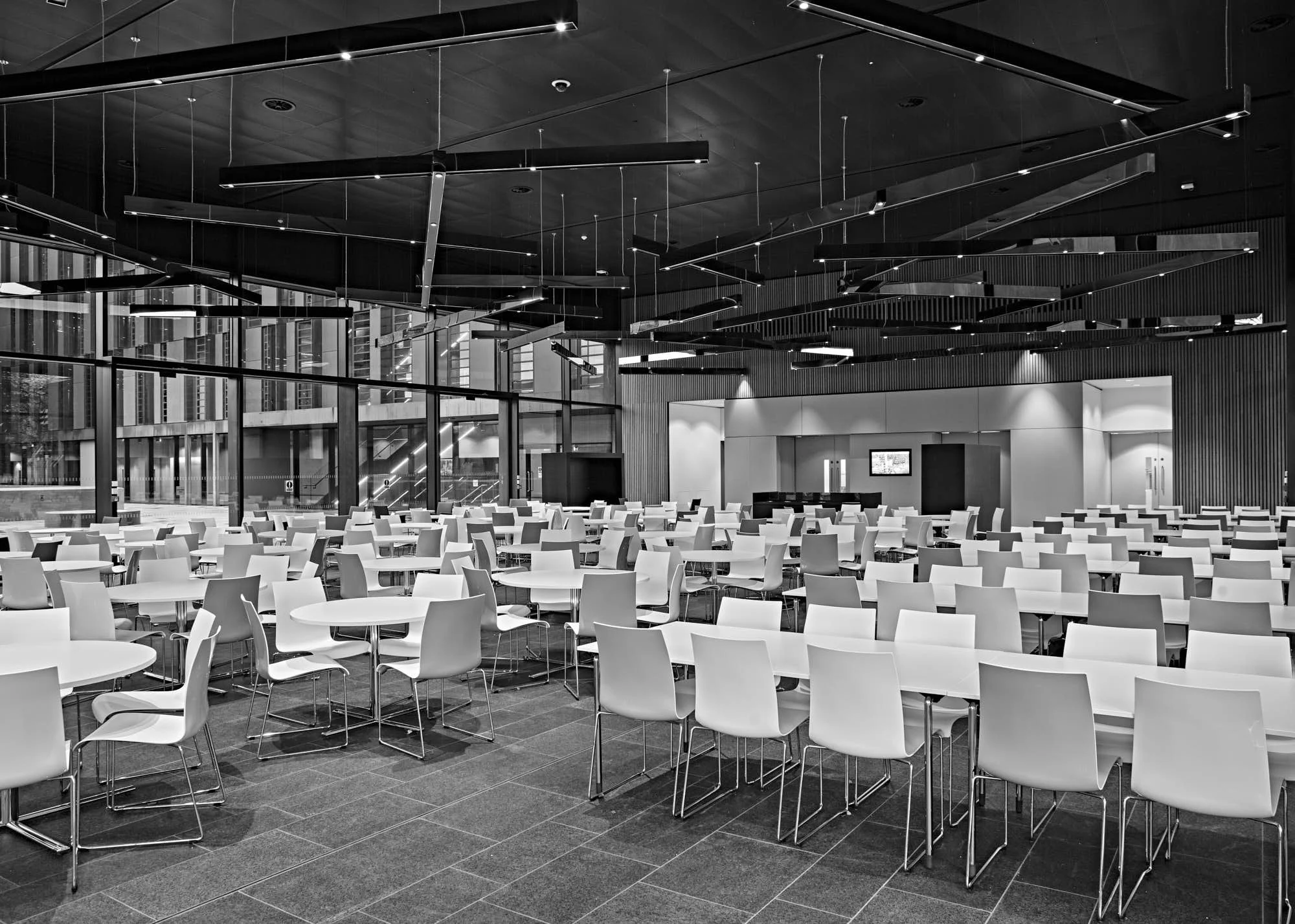 Modern interior space with white chairs and round tables, large glass windows, and contemporary lighting fixtures.