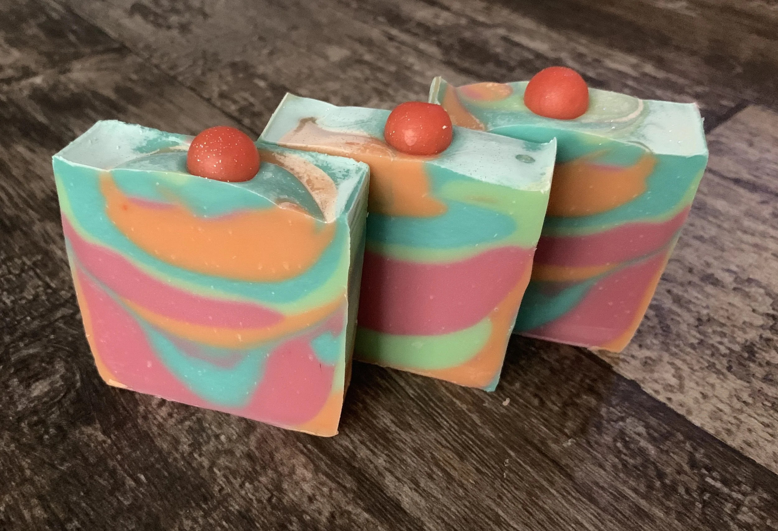Colorful marble-patterned soap bars topped with small round red soap decorations on a wooden surface.