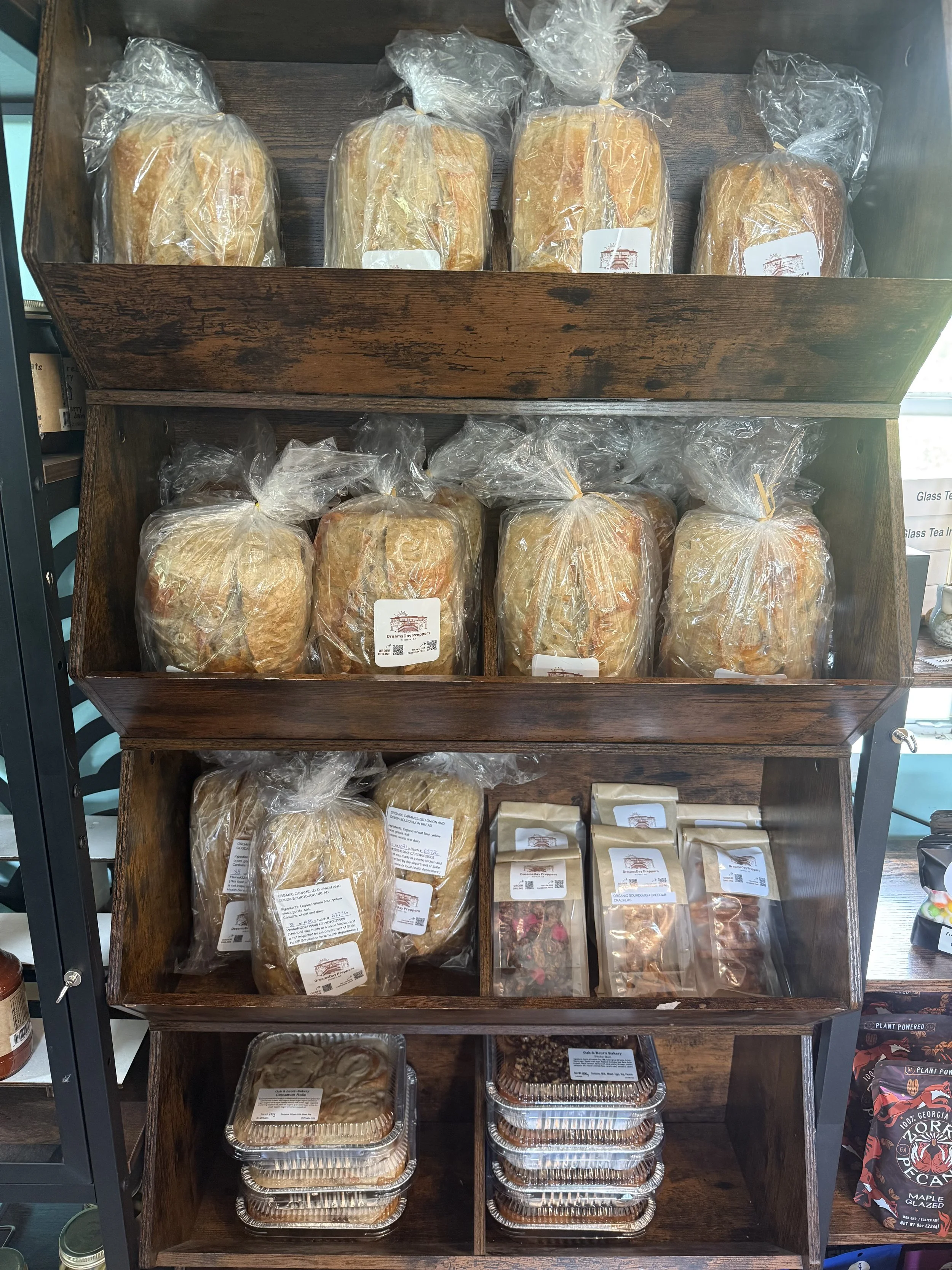 A wooden display shelf containing various baked goods, including bread and crackers, wrapped in plastic and served in aluminum trays.