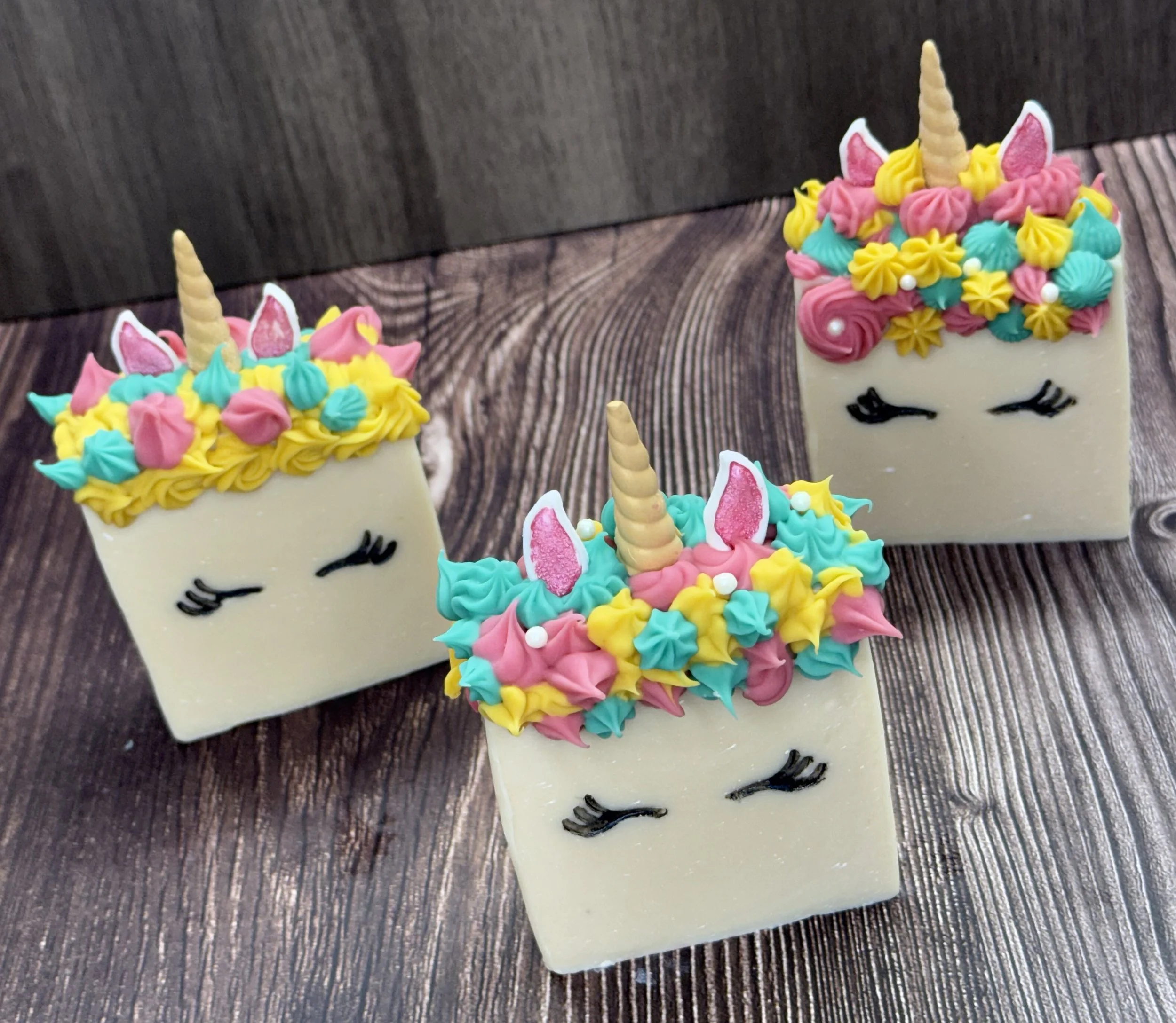 Decorative unicorn-themed cupcakes with colorful frosting, unicorn horns, and ears, on a wooden surface.