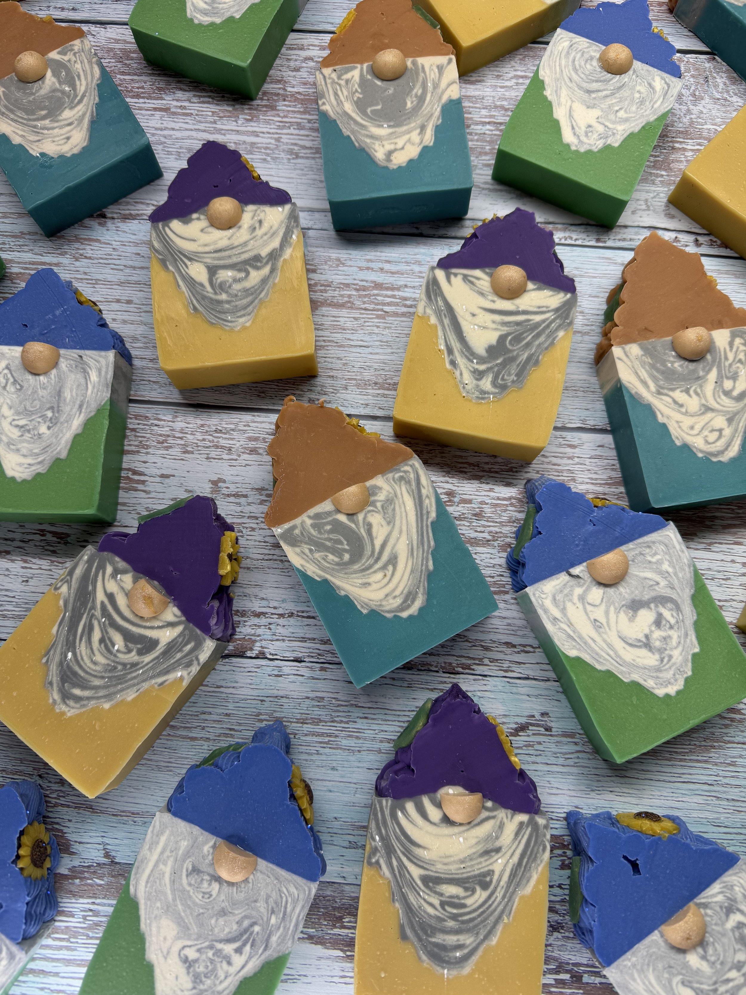 Colorful rectangular soaps with swirl patterns and small round embellishments on top, arranged on a wooden surface.