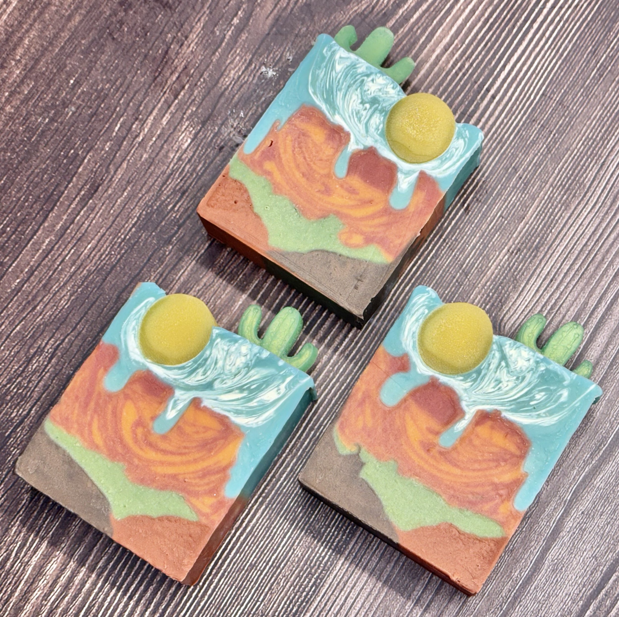 Colorful handcrafted soap on a wooden surface, decorated with yellow round accents and marbled blue, green, and orange patterns.