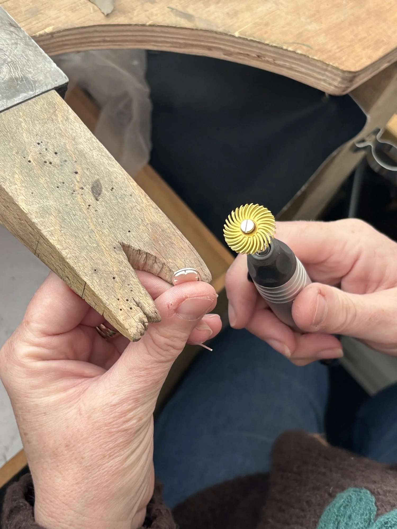 Person holding a small rotary tool with a yellow abrasive head, working on a wooden piece, in a workshop or craft space with a dark background.