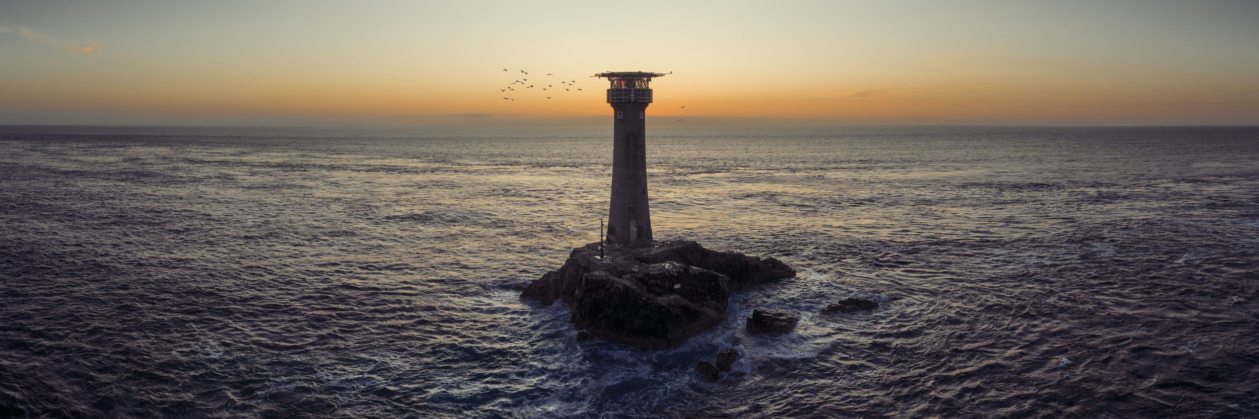 Lighthouse on a rocky outcrop at sea during dusk, evoking steady direction through change.