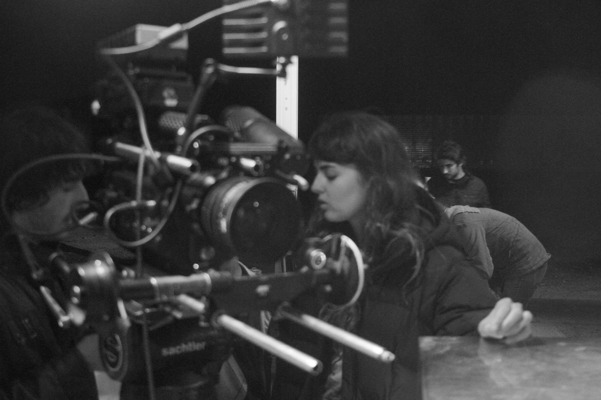 Black and white photo of film or video production crew working on a set with film equipment, and two individuals in the scene.