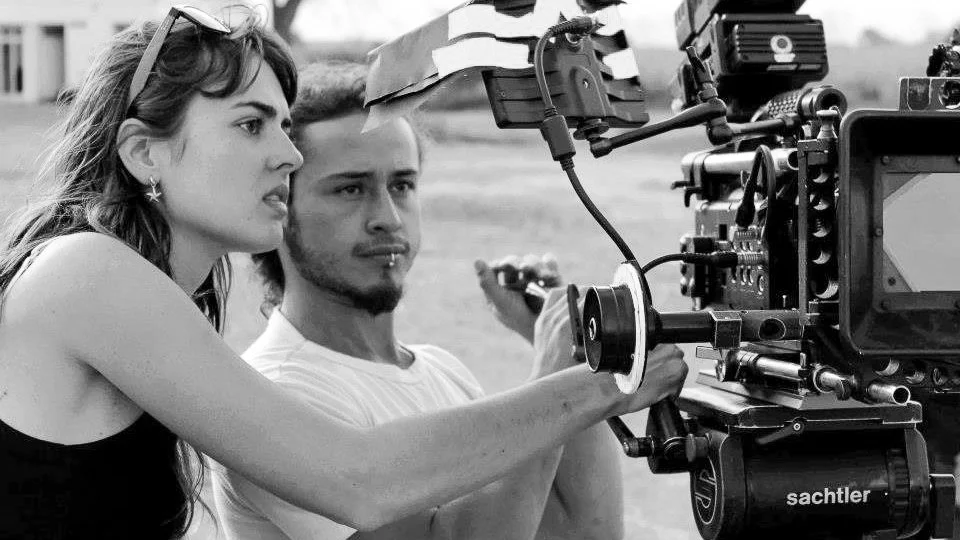 Two film crew members, a woman and a man, operate a professional video camera on set outdoors.