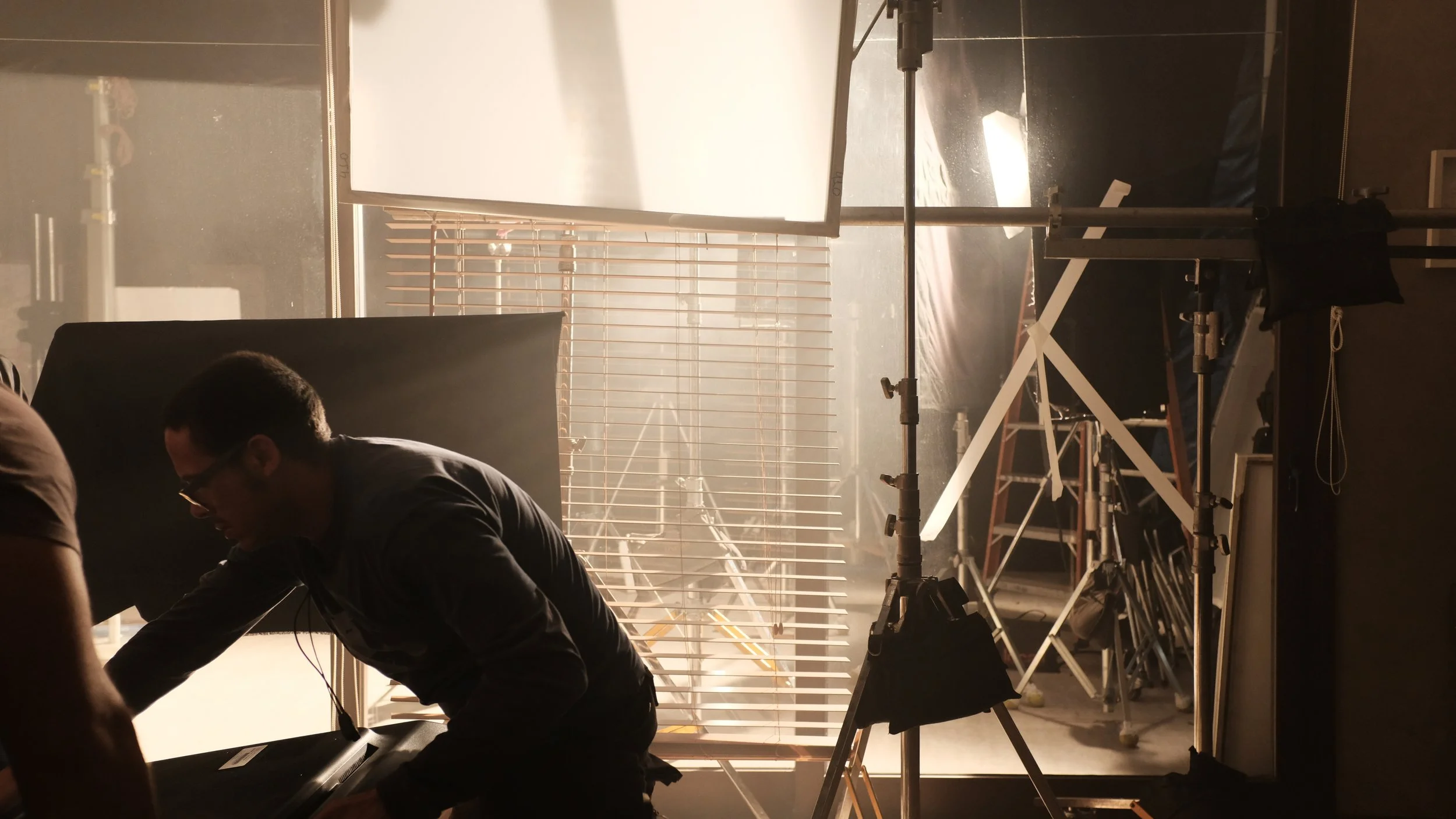 Behind the scenes of a photoshoot or film set with professional lighting, equipment, and crew members working.