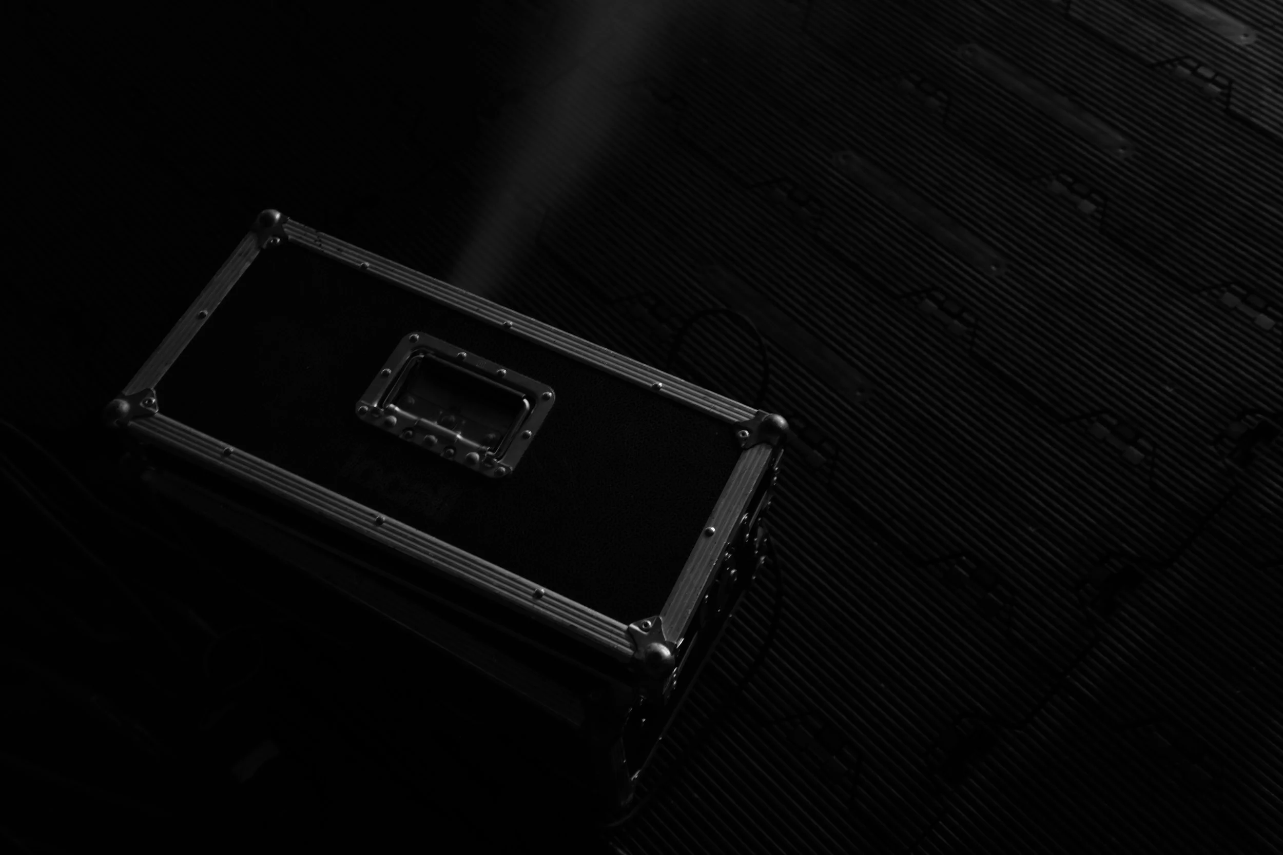 Black flight case with metal reinforcements on dark textured surface.
