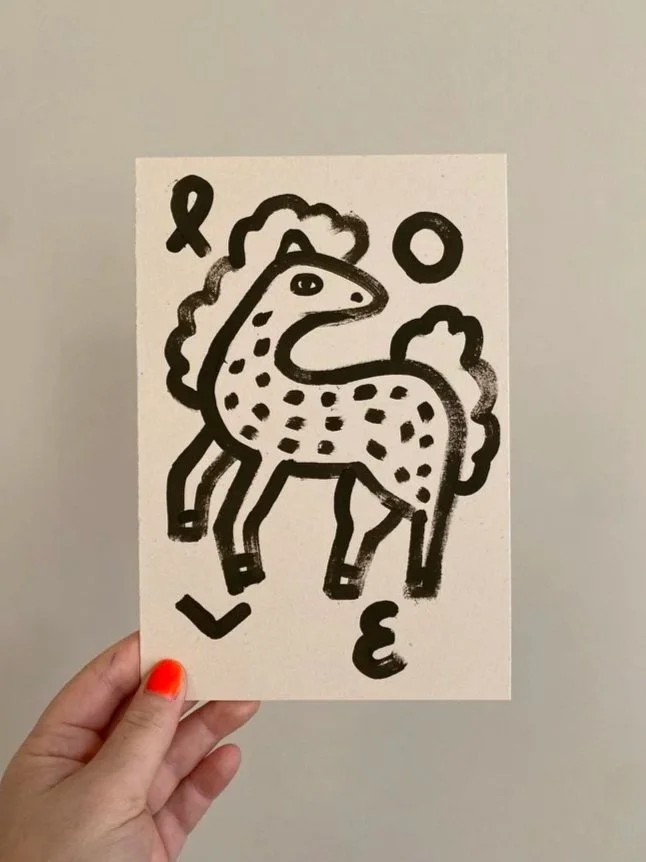 Eine Hand hält ein Schwarz-Weiß-Gemälde eines stilisierten Einhorns mit den Buchstaben L O V E, love