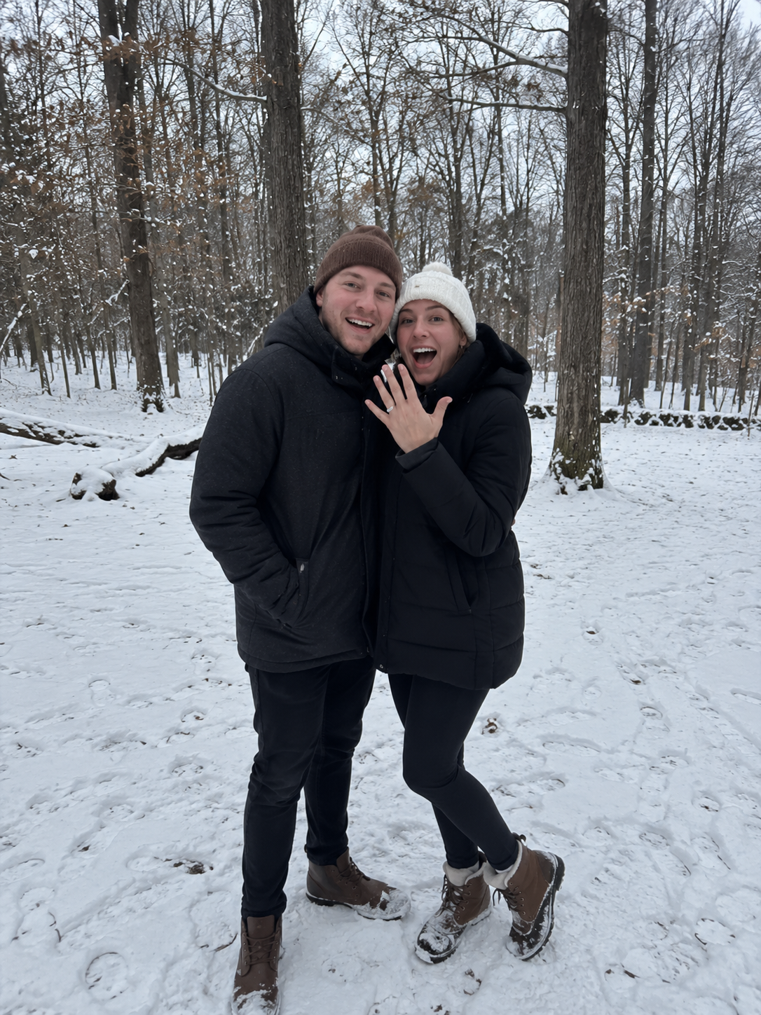 Couple celebrating their engagement in a snowy forest, showcasing a bespoke diamond engagement ring. Romantic proposal photography capturing love, commitment and handcrafted bridal jewellery.