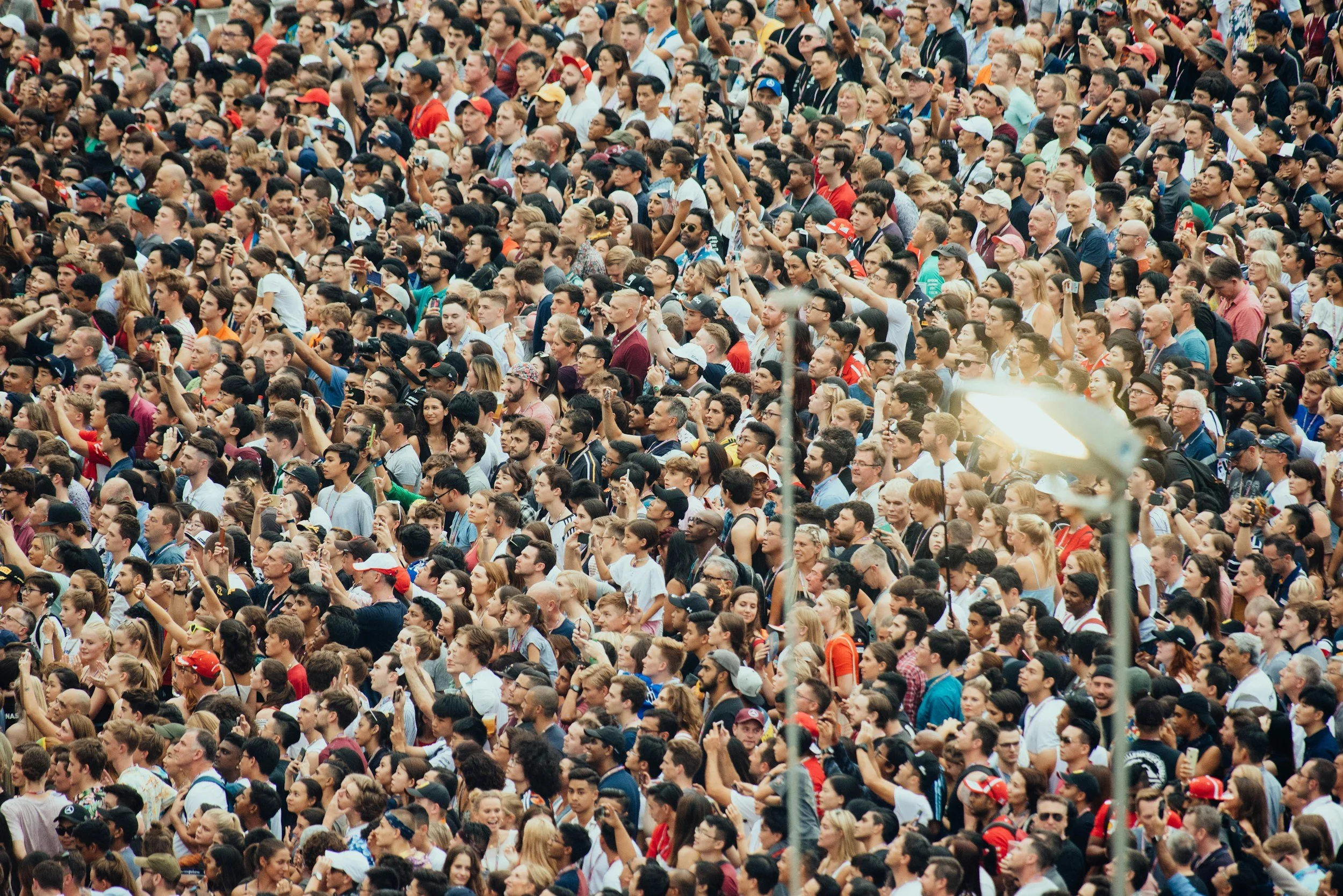 Crowd of people attending an outdoor event, many holding up smartphones to take photos or videos.