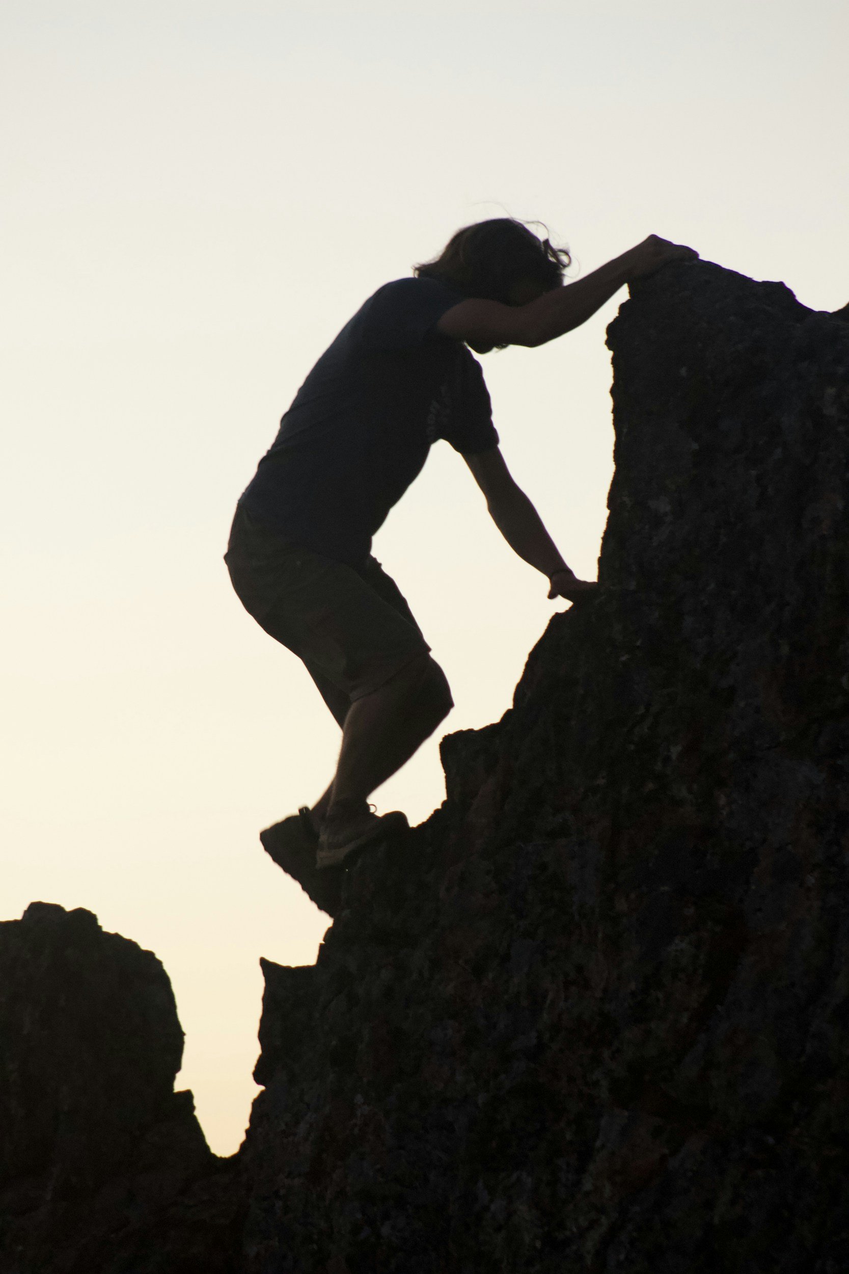 A person climbing on rocks at sunset or sunrise.
