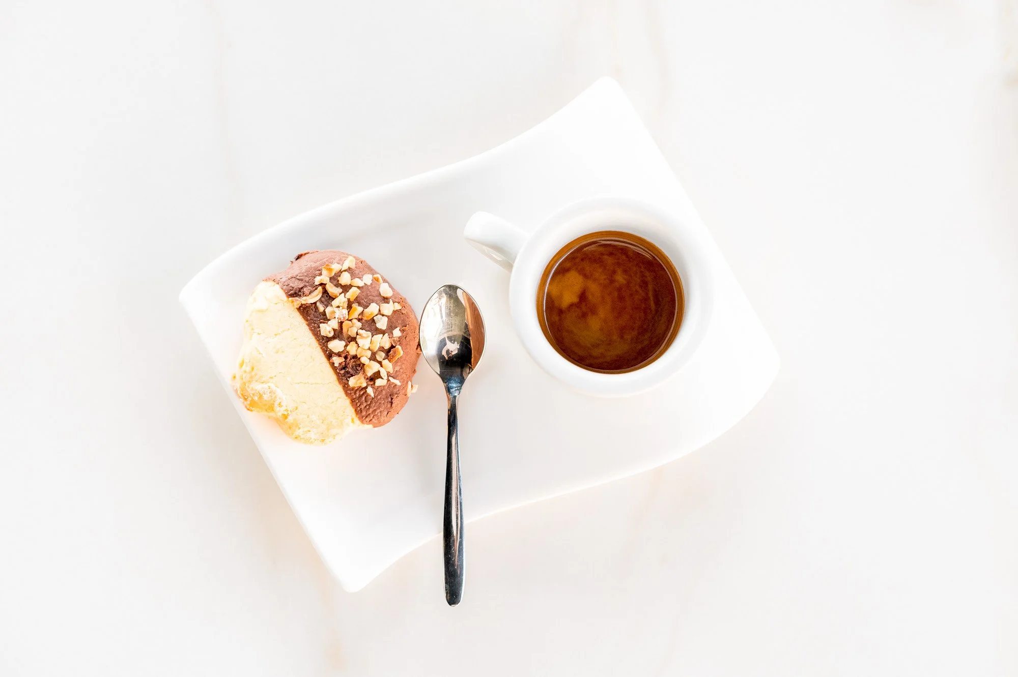Panna cotta con cioccolato e nocciole, tazza di tè nero, cucchiaio, piatto bianco, sfondo bianco