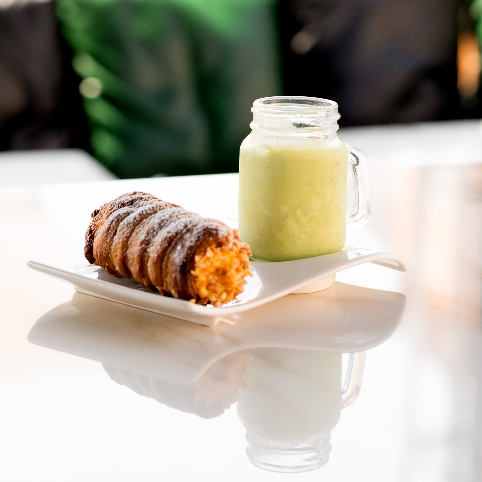 Una bevanda verde in una tazza di vetro con manico, circondata da biscotti ricoperti di zucchero a velo, su un piatto bianco.
