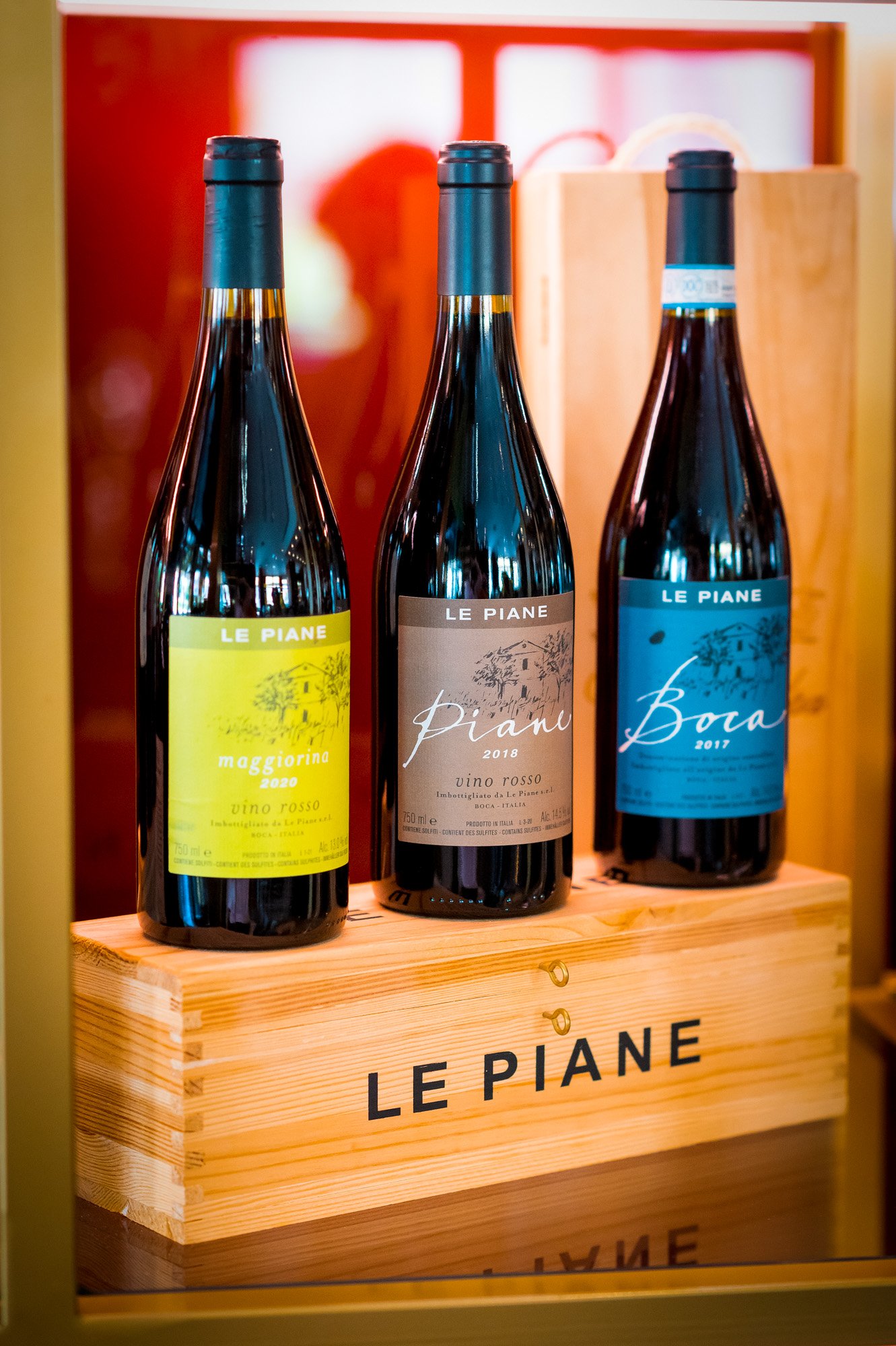 Tre bottiglie di vino rosso sulla mensola di legno con etichette colorate e il marchio "Le Piane" in primo piano.